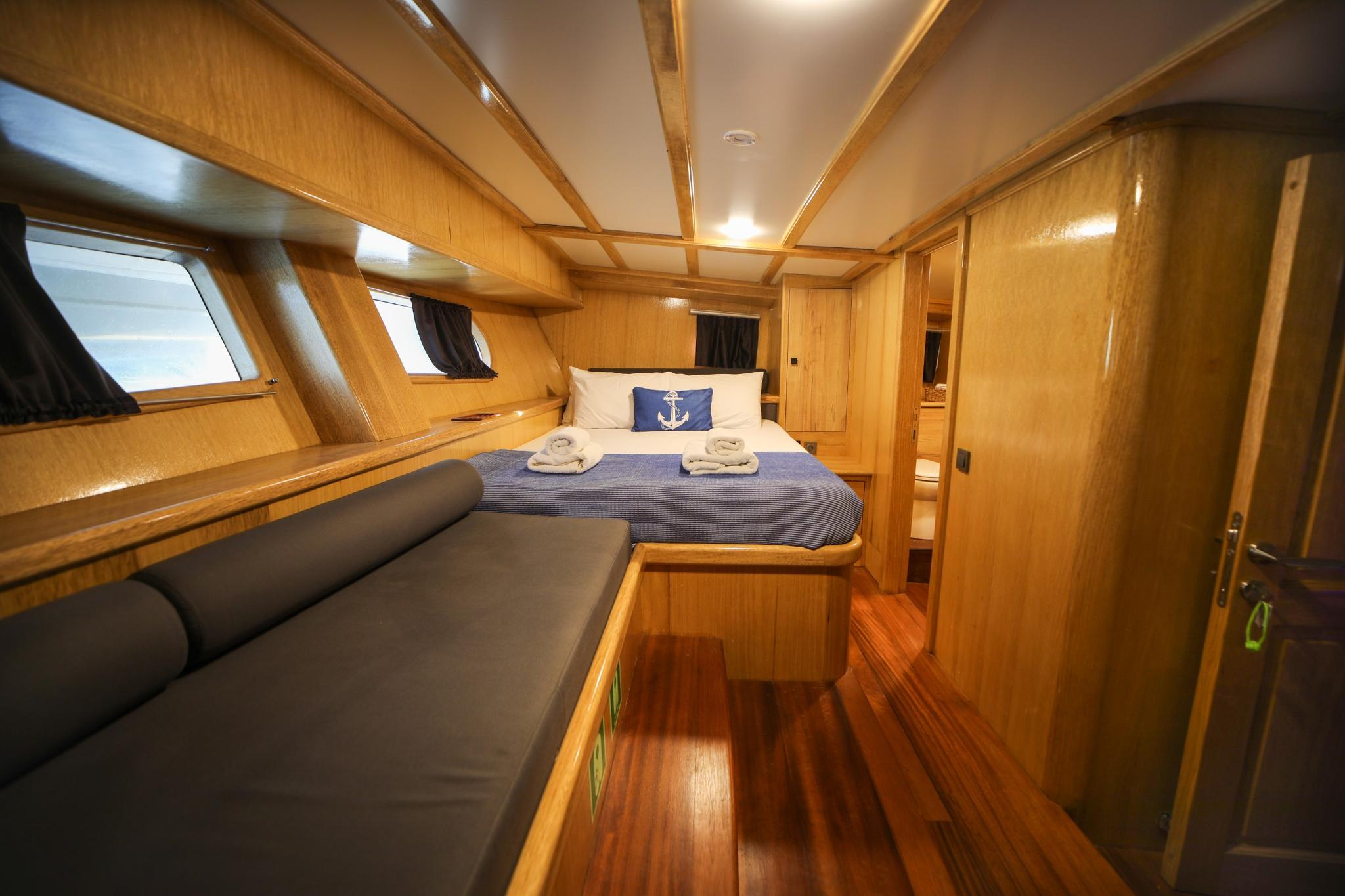 yacht guest cabin with double bed, striped bedding, nautical pillow, gray seating area and wooden finishes