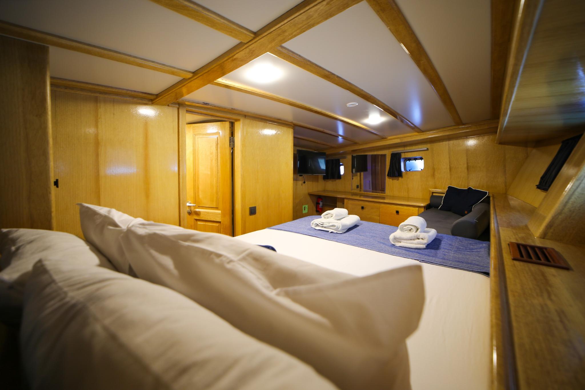 guest cabin interior with double bed, white linens, towels, wooden paneling and small TV
