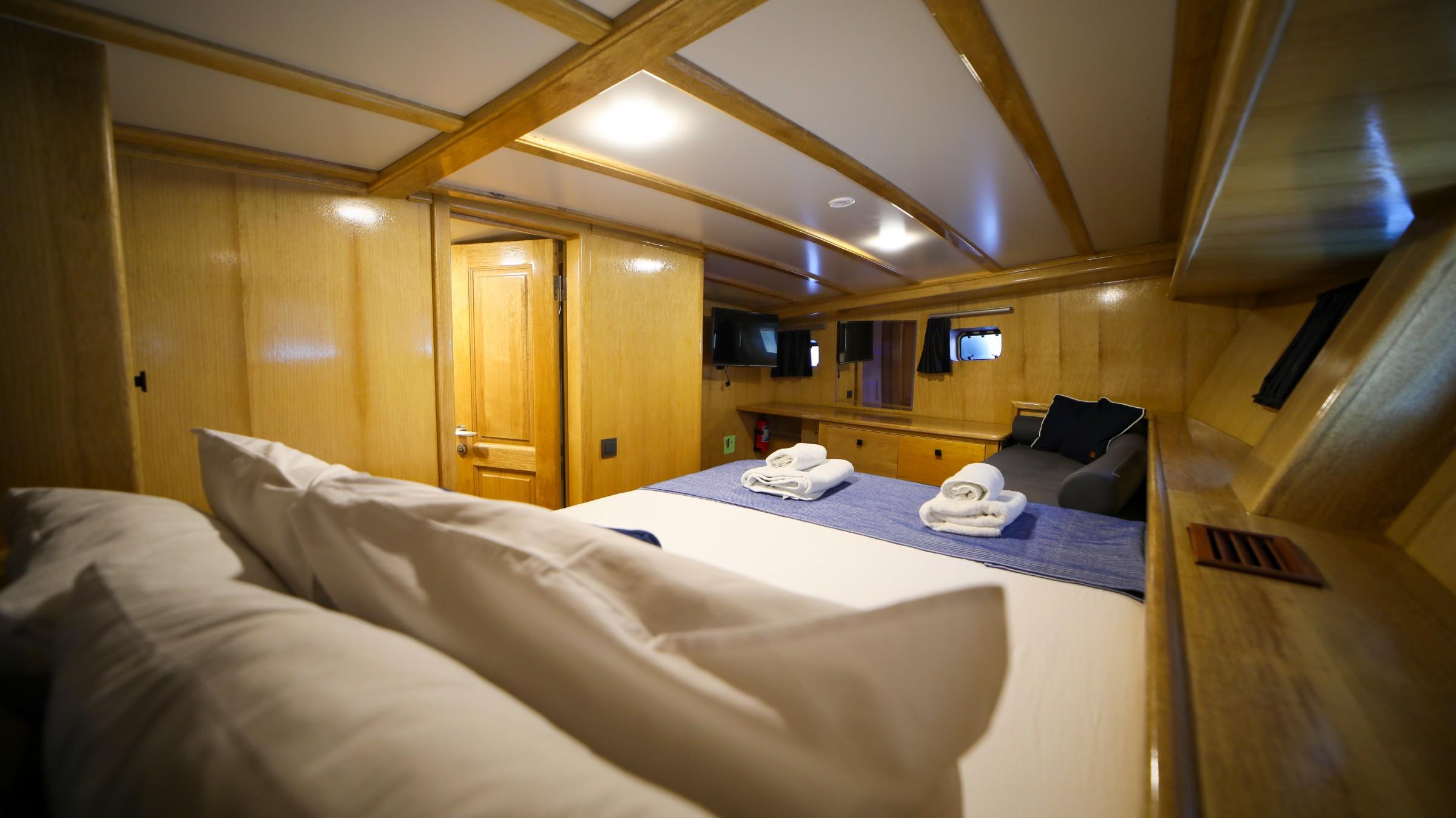 yacht guest cabin featuring double bed with blue runner, wooden paneling and built-in storage