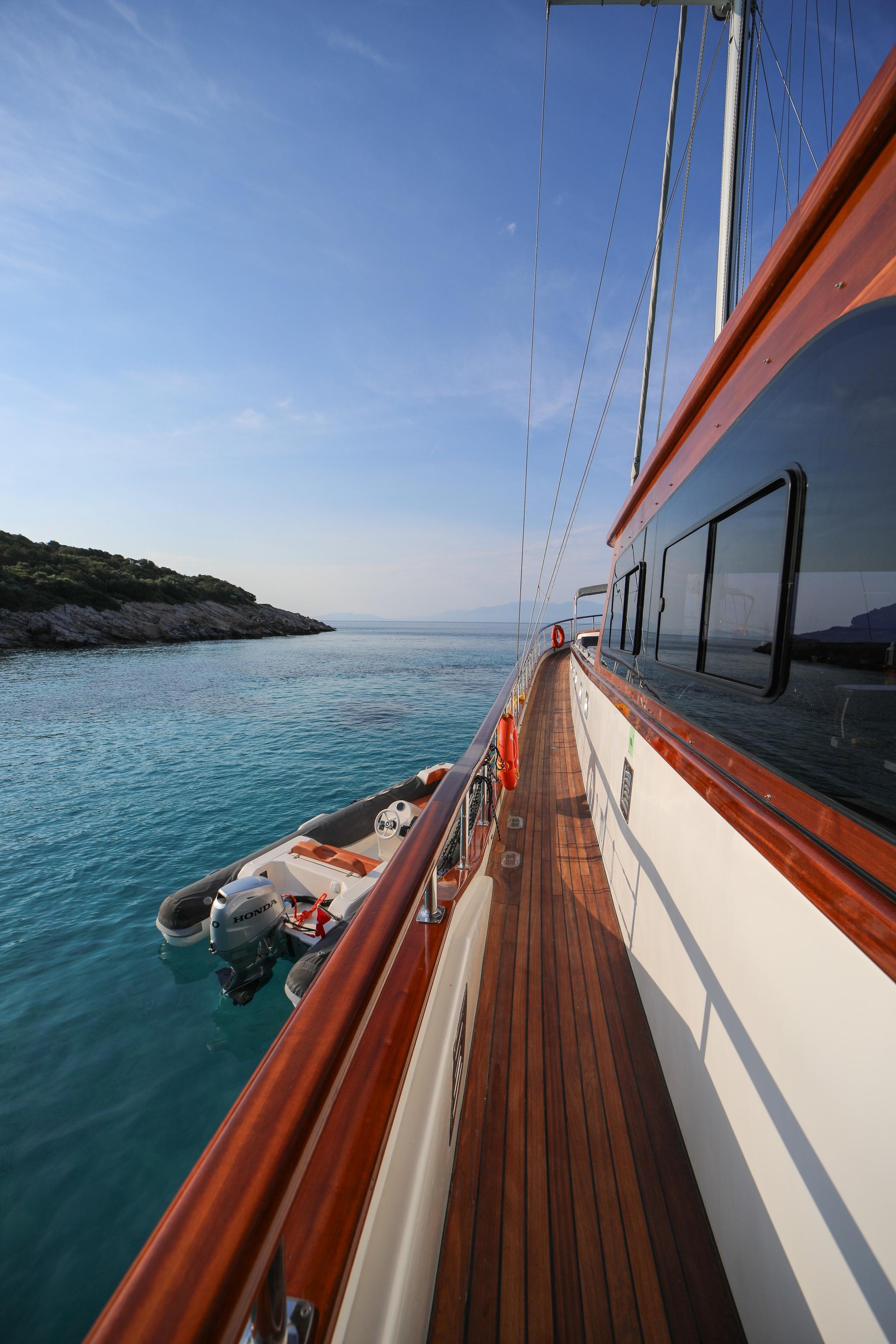 Gulet side deck with teak planking, white hull, rigging and tender alongside in turquoise bay