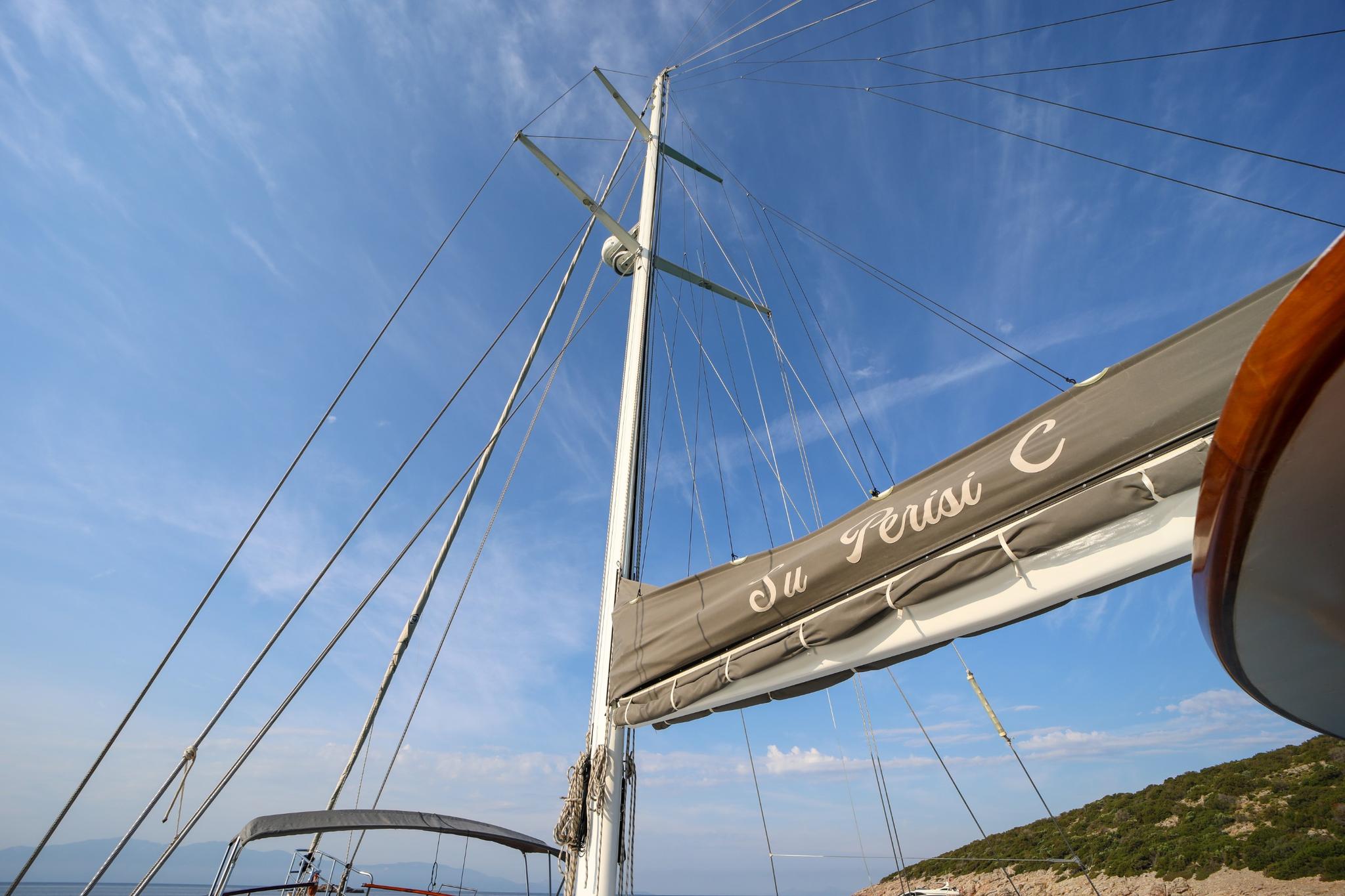 sailing yacht mast and boom with rigging against blue sky and coastline