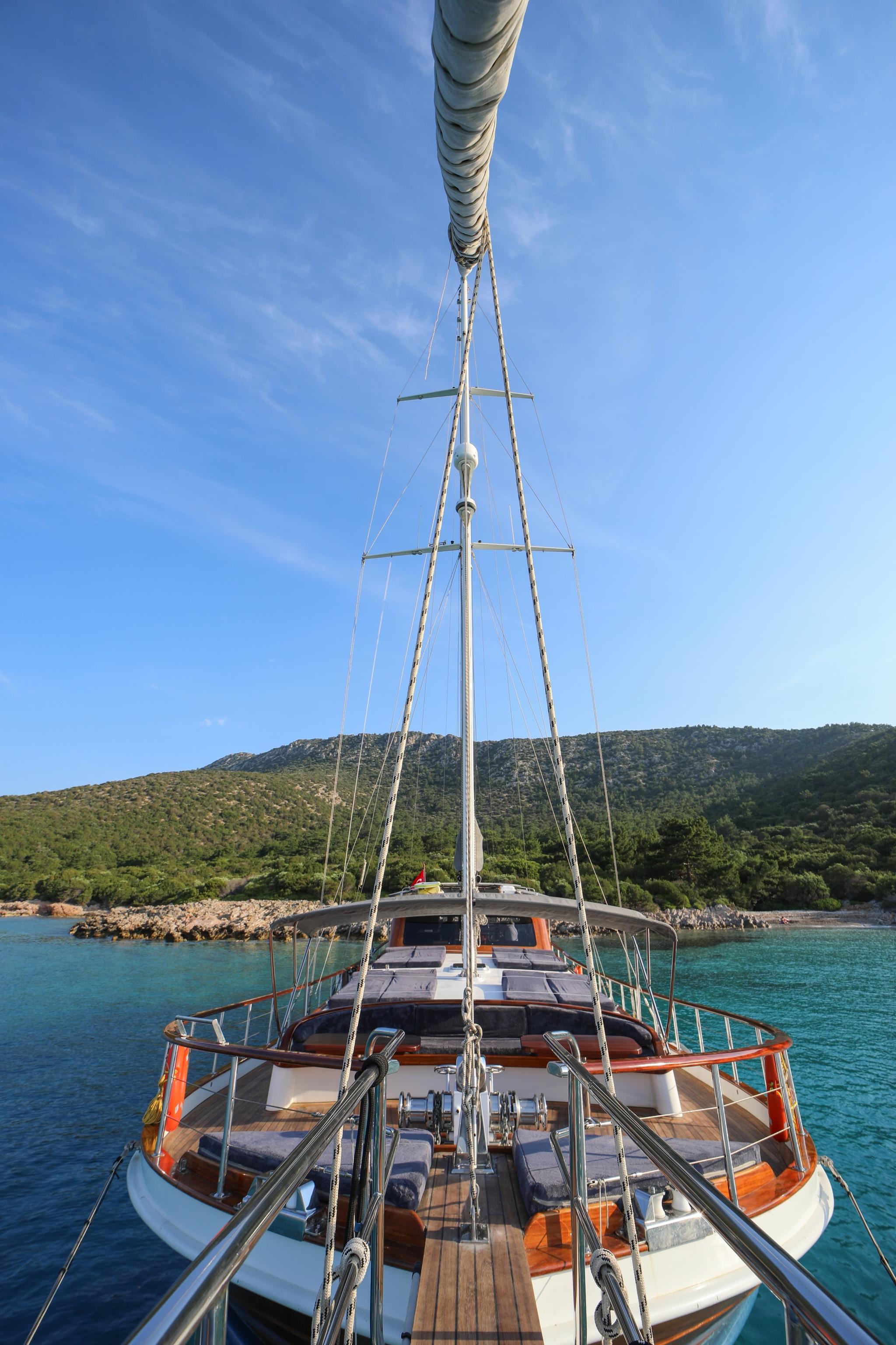 gulet stern deck showing wooden planking, mast with rigging, and Mediterranean coastline
