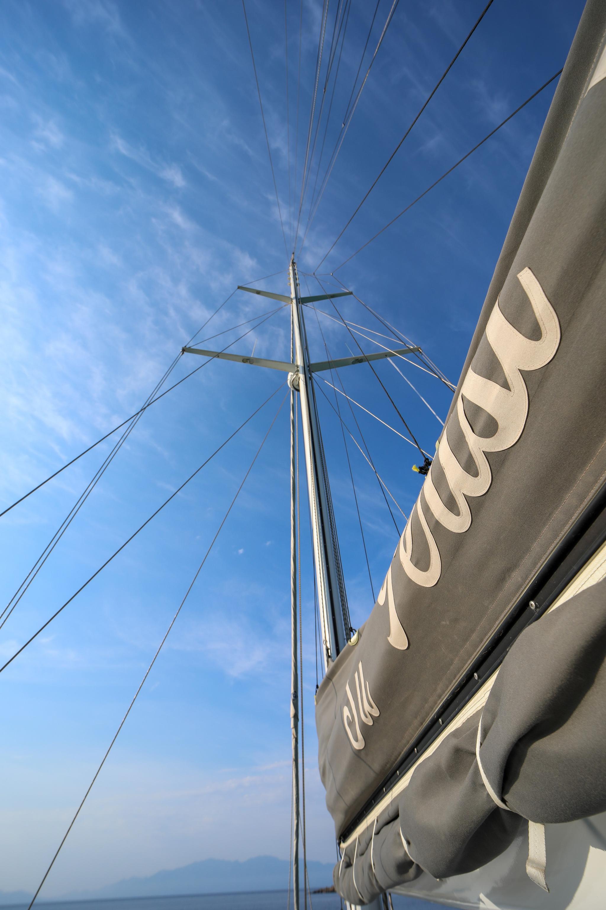 yacht mast with spreaders and rigging lines against blue sky with white clouds