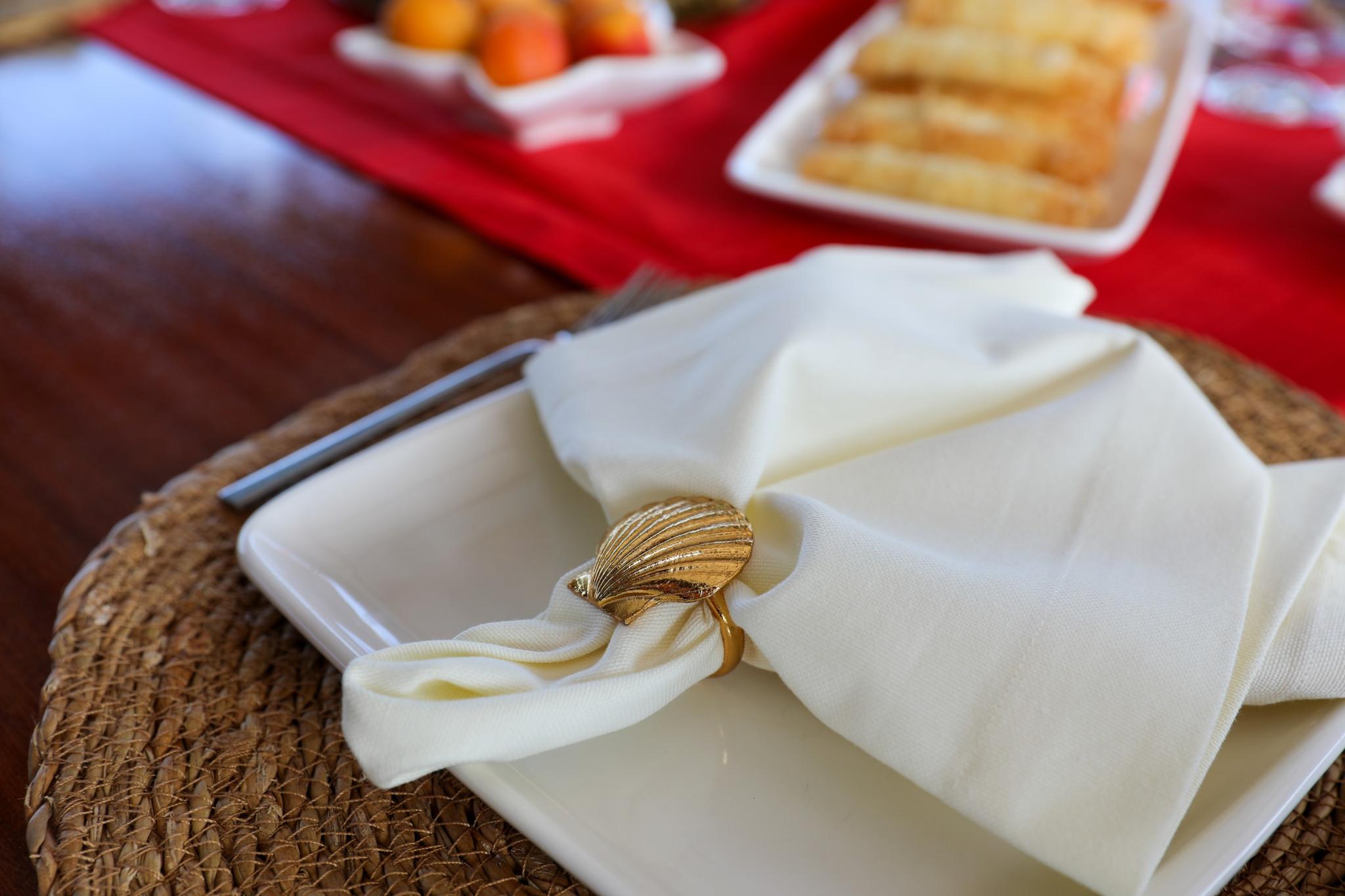 elegant white dinner plate with folded napkin secured by golden shell-shaped napkin ring