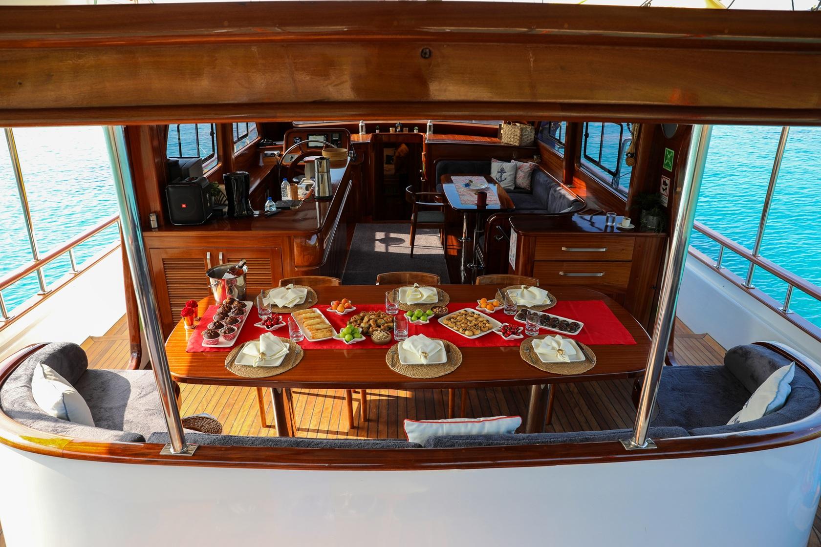 yacht dining table set with red tablecloth, appetizers, plates and glassware in salon