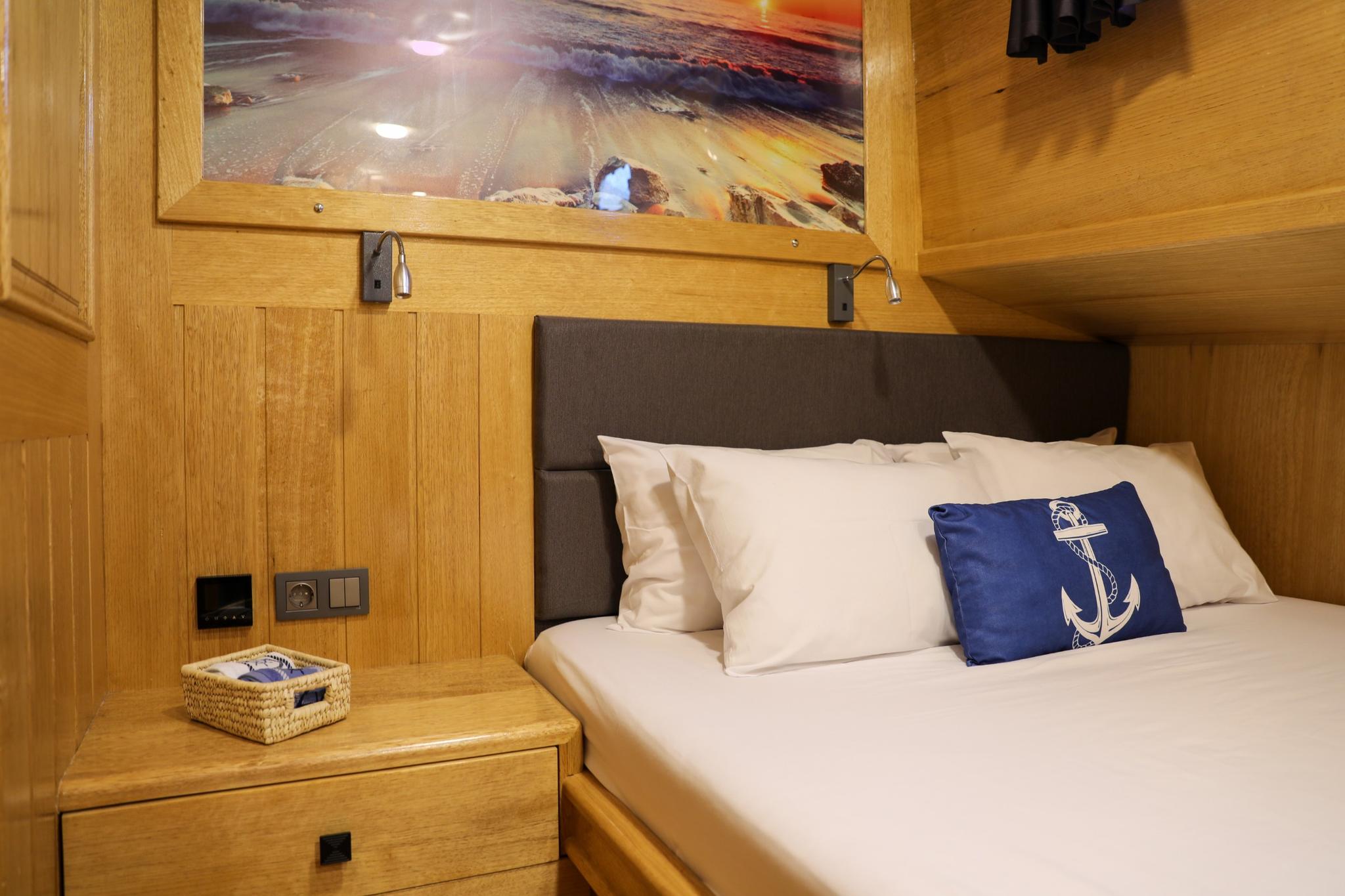 yacht guest cabin featuring double bed with white linens, navy anchor cushion, and warm wood paneling