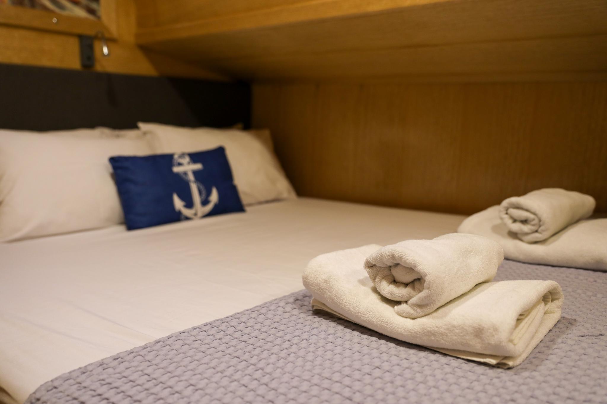 yacht guest cabin bed with white linens, blue anchor pillow and rolled towels