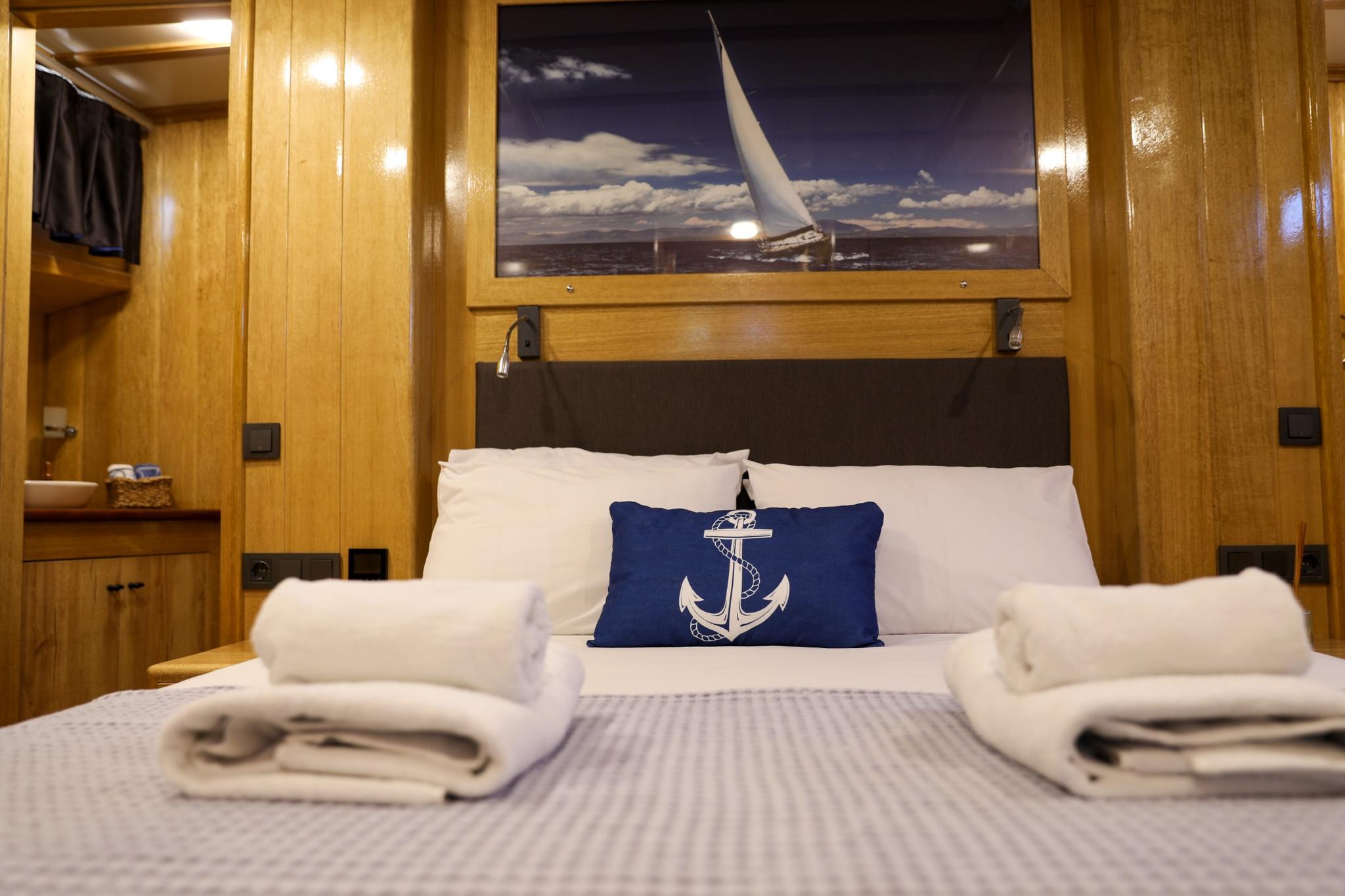 yacht guest cabin with double bed, white linens, nautical anchor pillow and sailing artwork