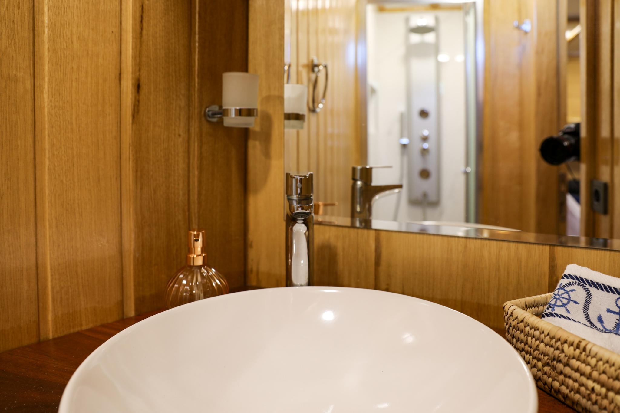 yacht bathroom featuring round white basin, chrome faucet, mirror and wooden paneling