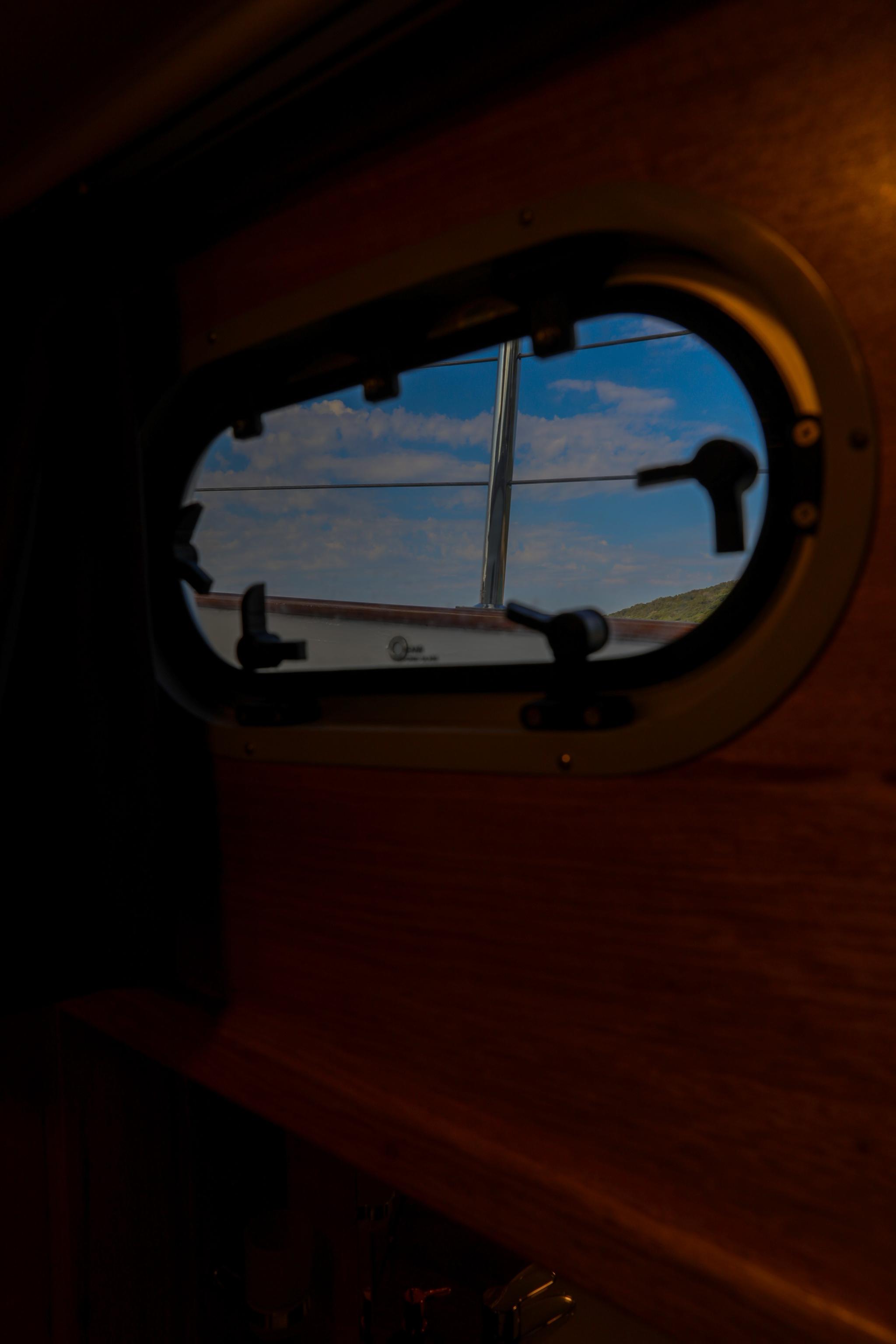 yacht cabin interior porthole window showing blue sky and coastline view