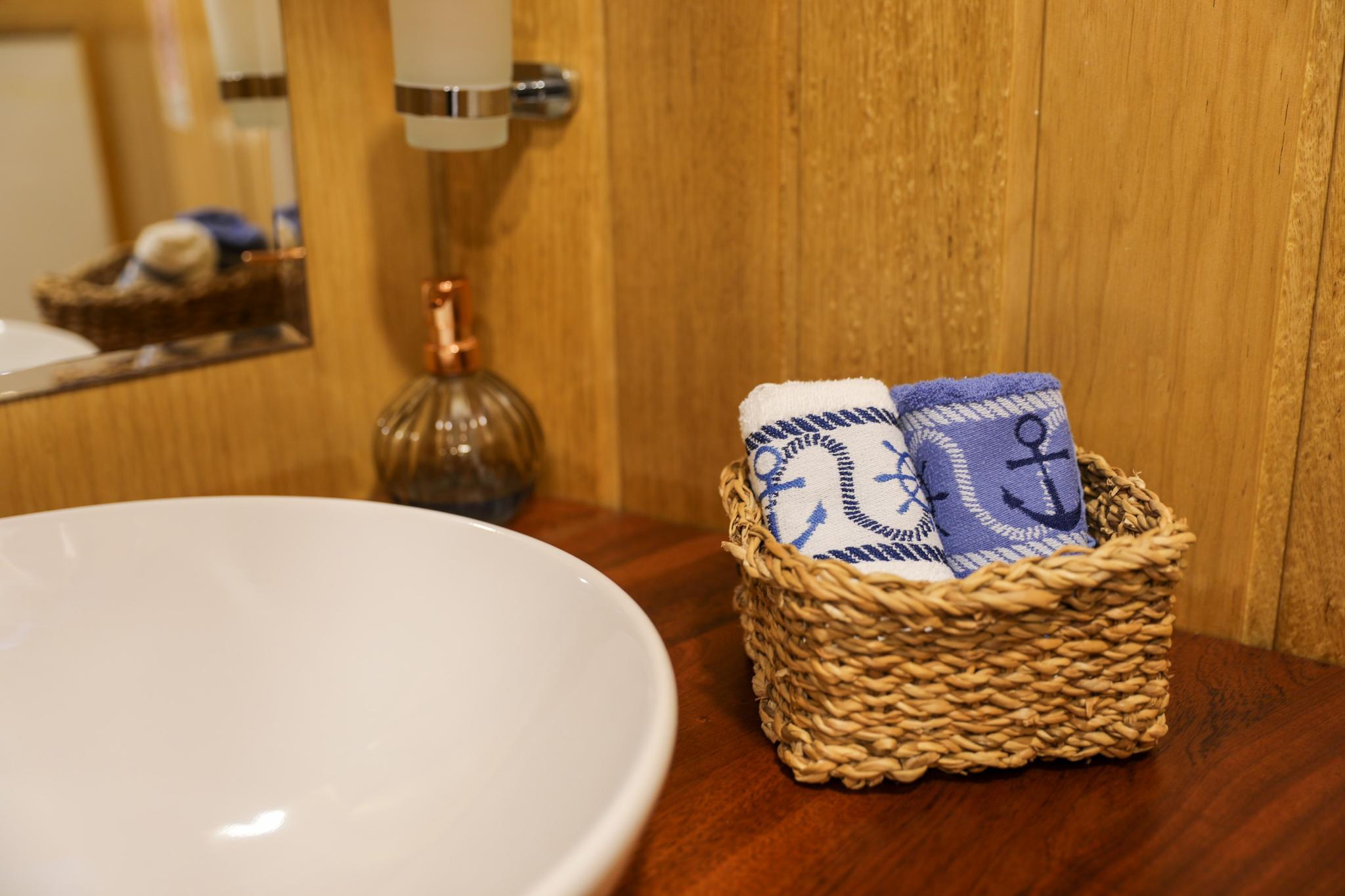 yacht bathroom vanity with white ceramic sink, nautical towels in wicker basket, wooden cabinetry