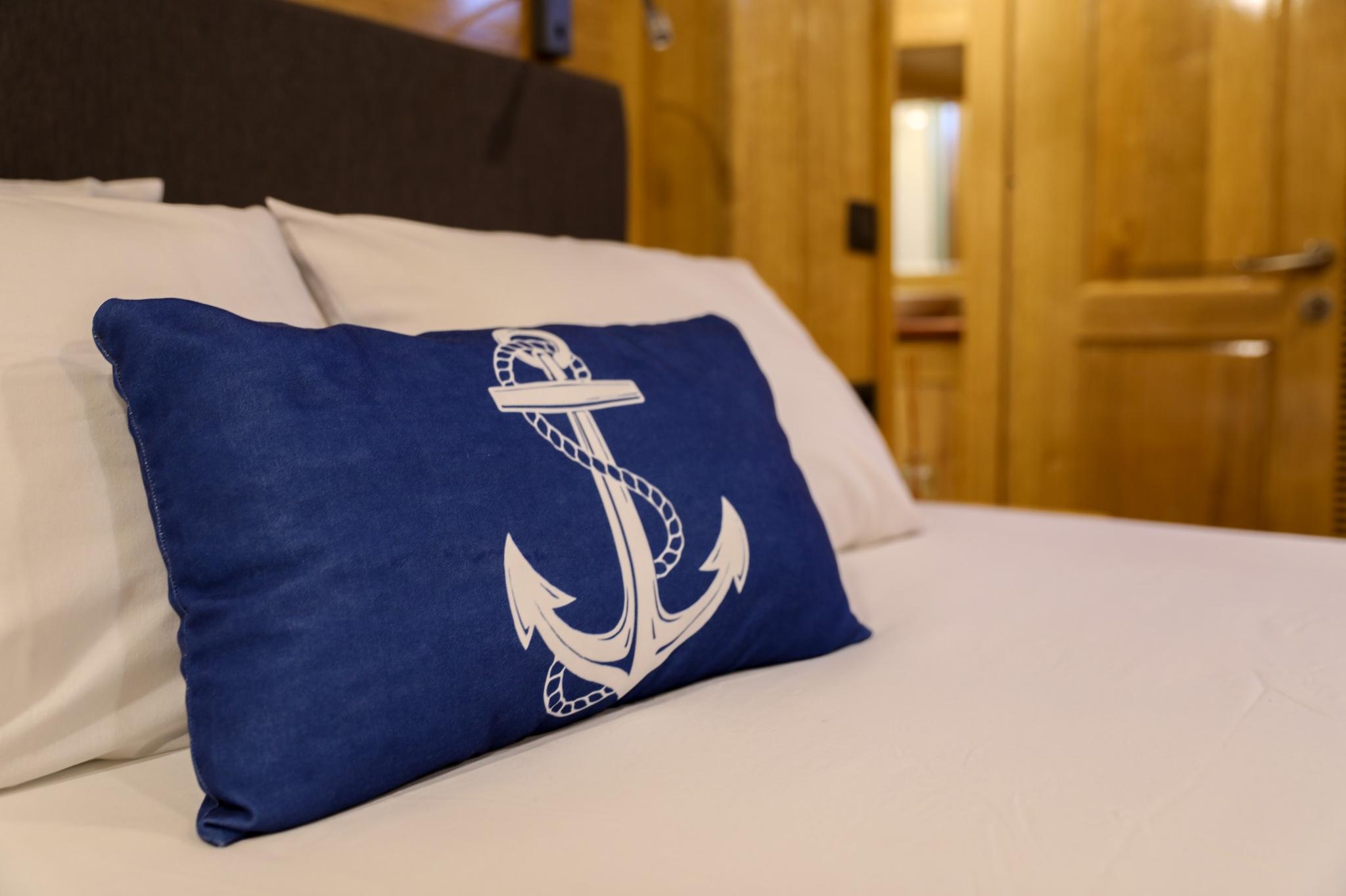 yacht guest cabin featuring white bedding with blue nautical anchor pillow and wood paneling