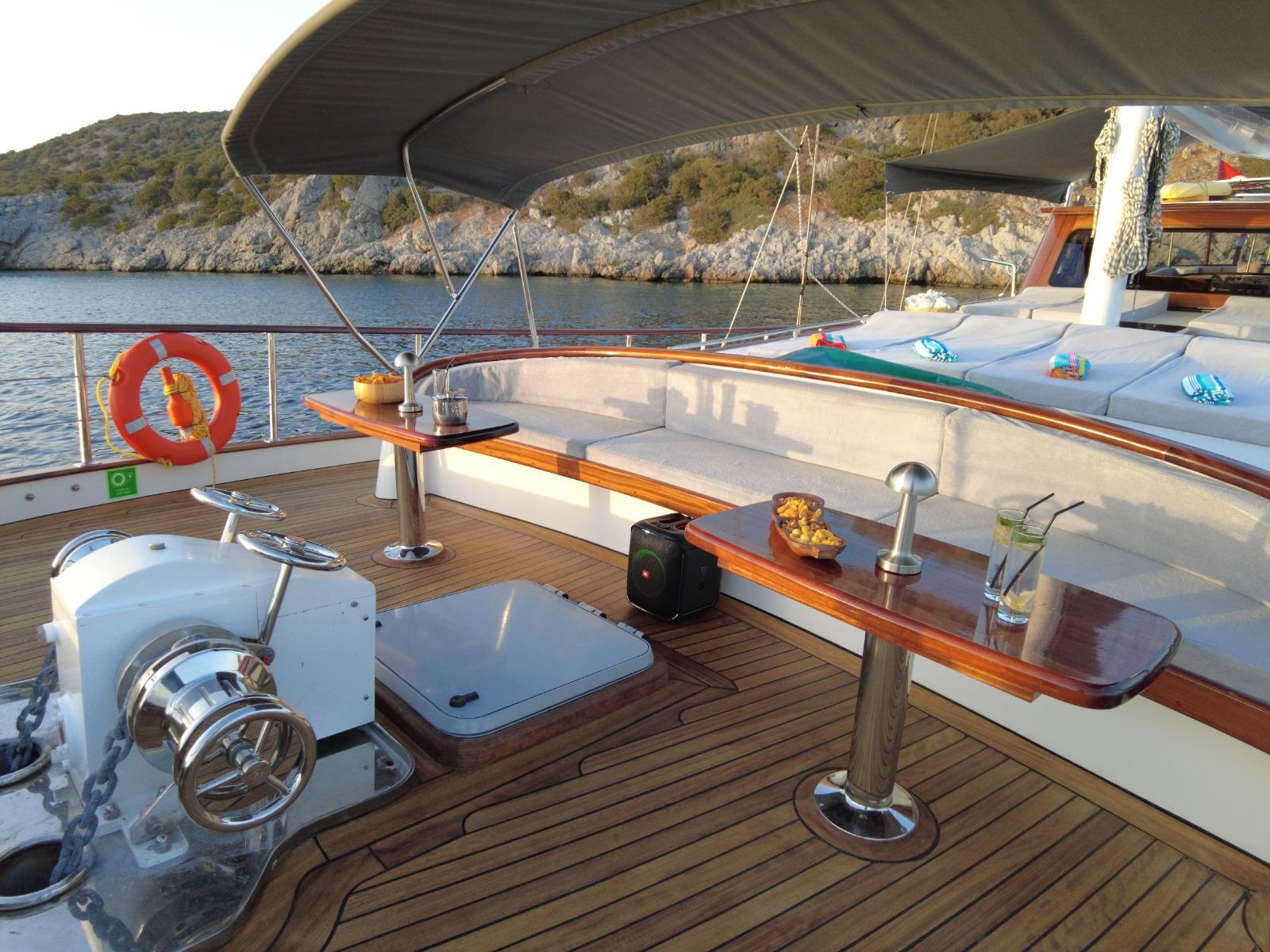 yacht aft deck with white cushioned seating, wooden dining table and helm station at anchor