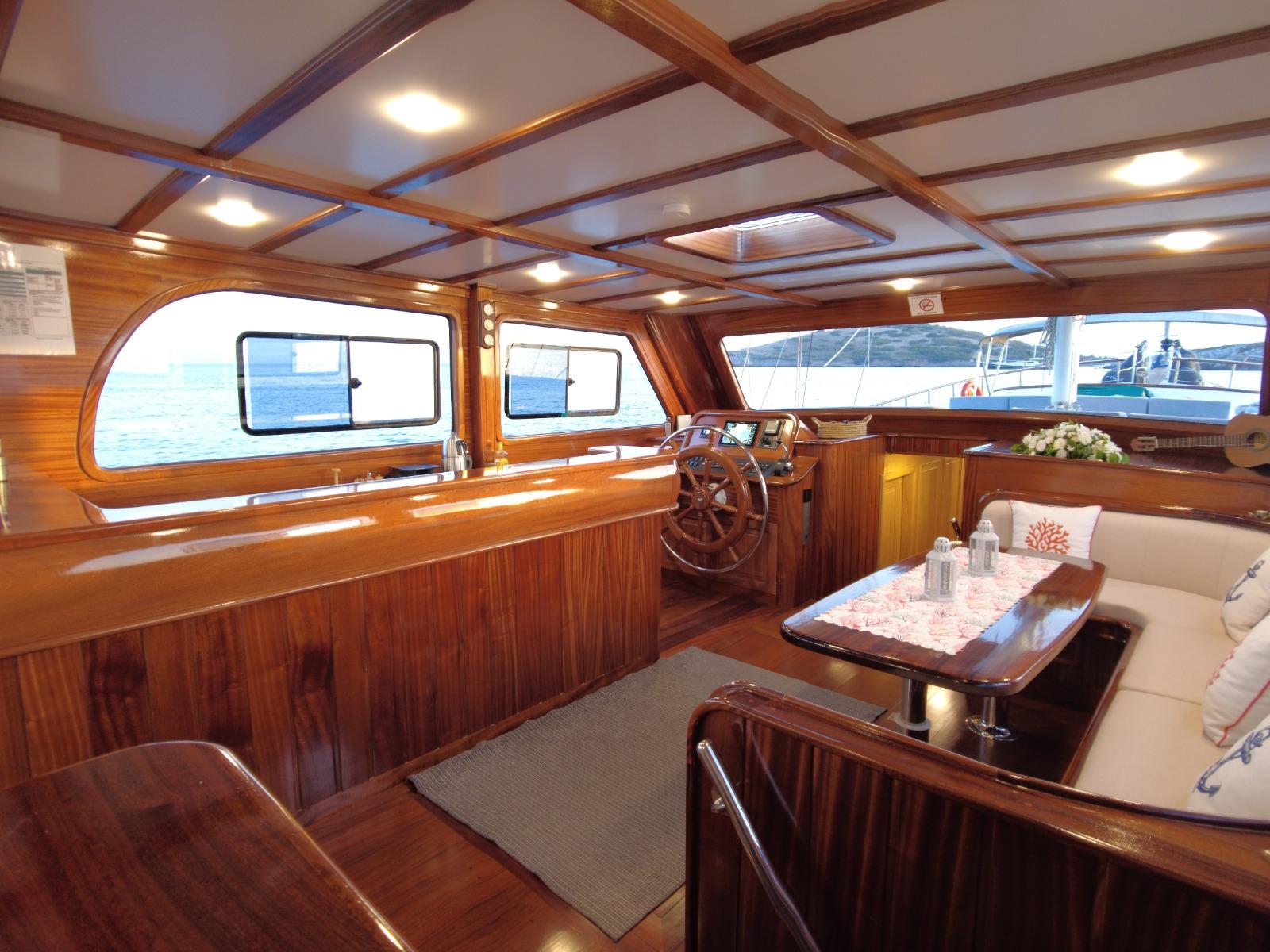 yacht interior salon with wooden dining table, helm wheel, and panoramic windows