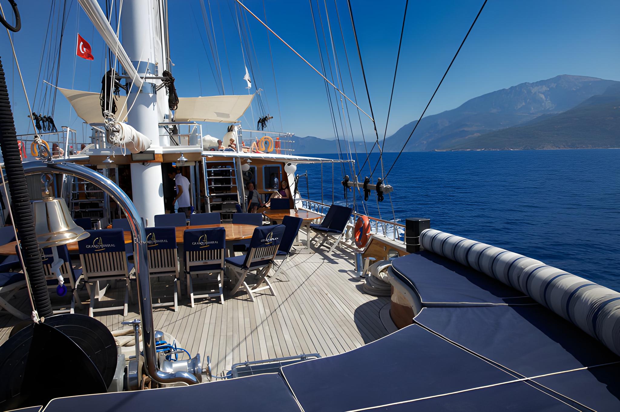 gulet main deck with outdoor dining table, teak decking, and mountainous coastline views