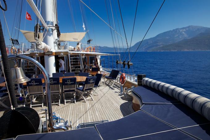 gulet main deck with outdoor dining table, teak decking, and mountainous coastline views