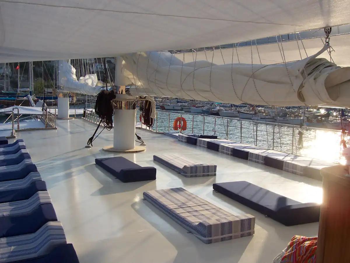 yacht deck lounge with striped cushioned seating under white canvas awning with sailing rigging