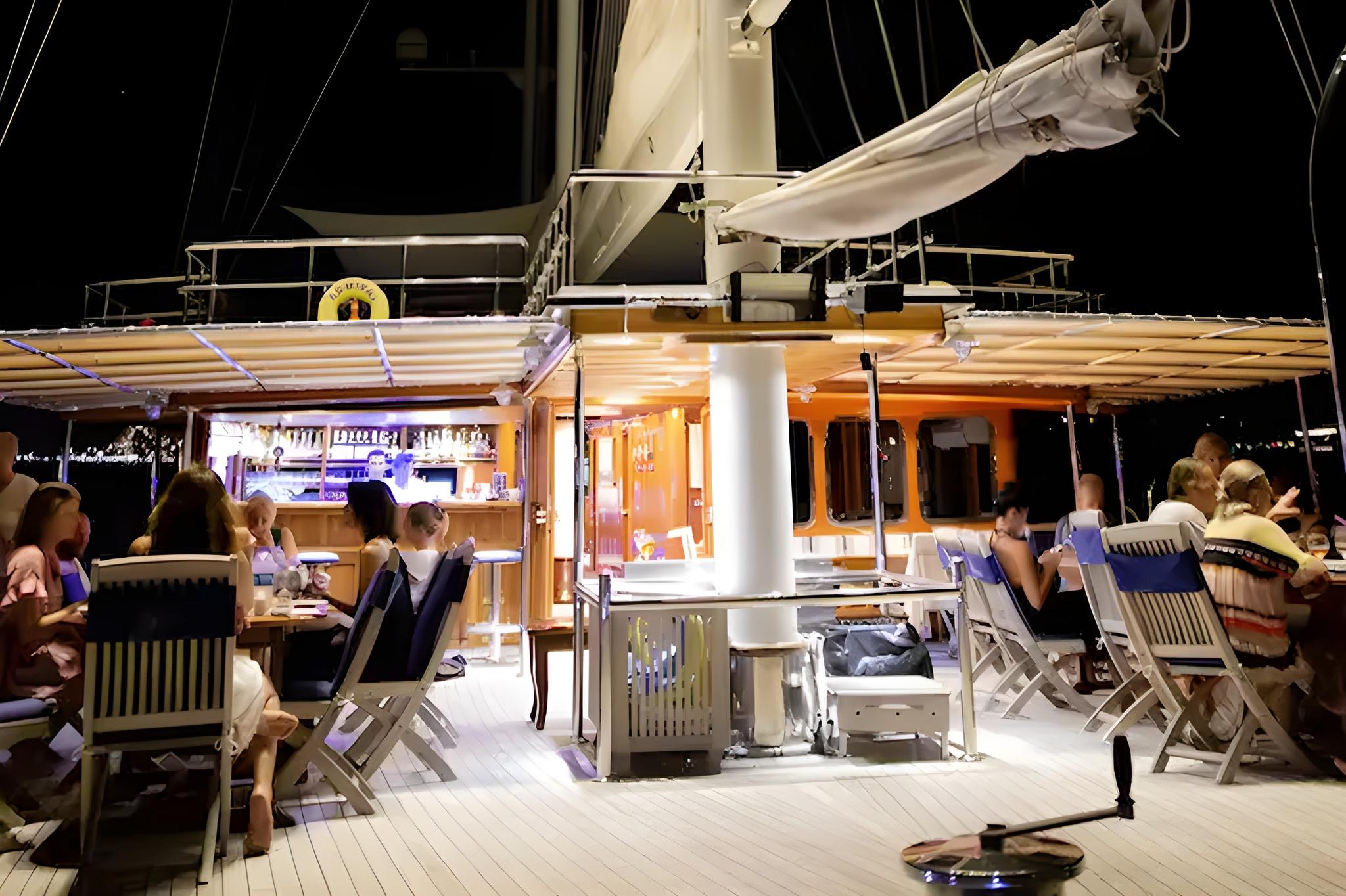 yacht aft deck with dining table, lounge seating, and guests relaxing at night
