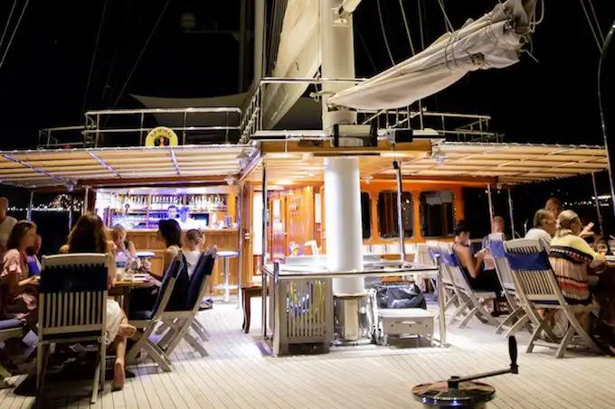 yacht aft deck with dining table, lounge seating, and guests relaxing at night