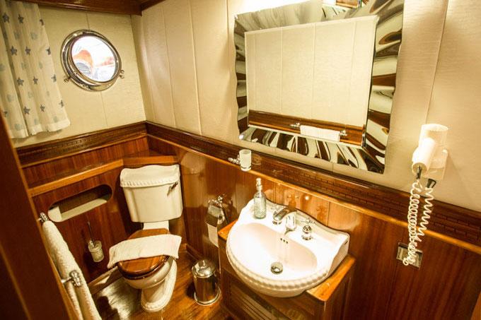 yacht bathroom interior with white toilet, round sink, mirror and wood paneling