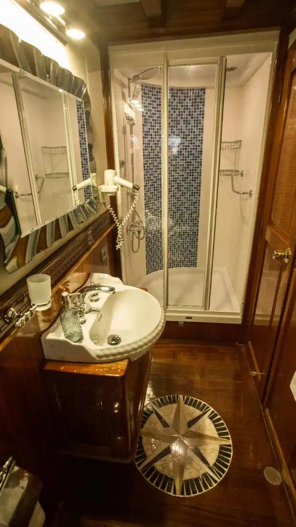 yacht bathroom featuring white vanity basin, glass shower enclosure with mosaic tile wall, and wooden flooring