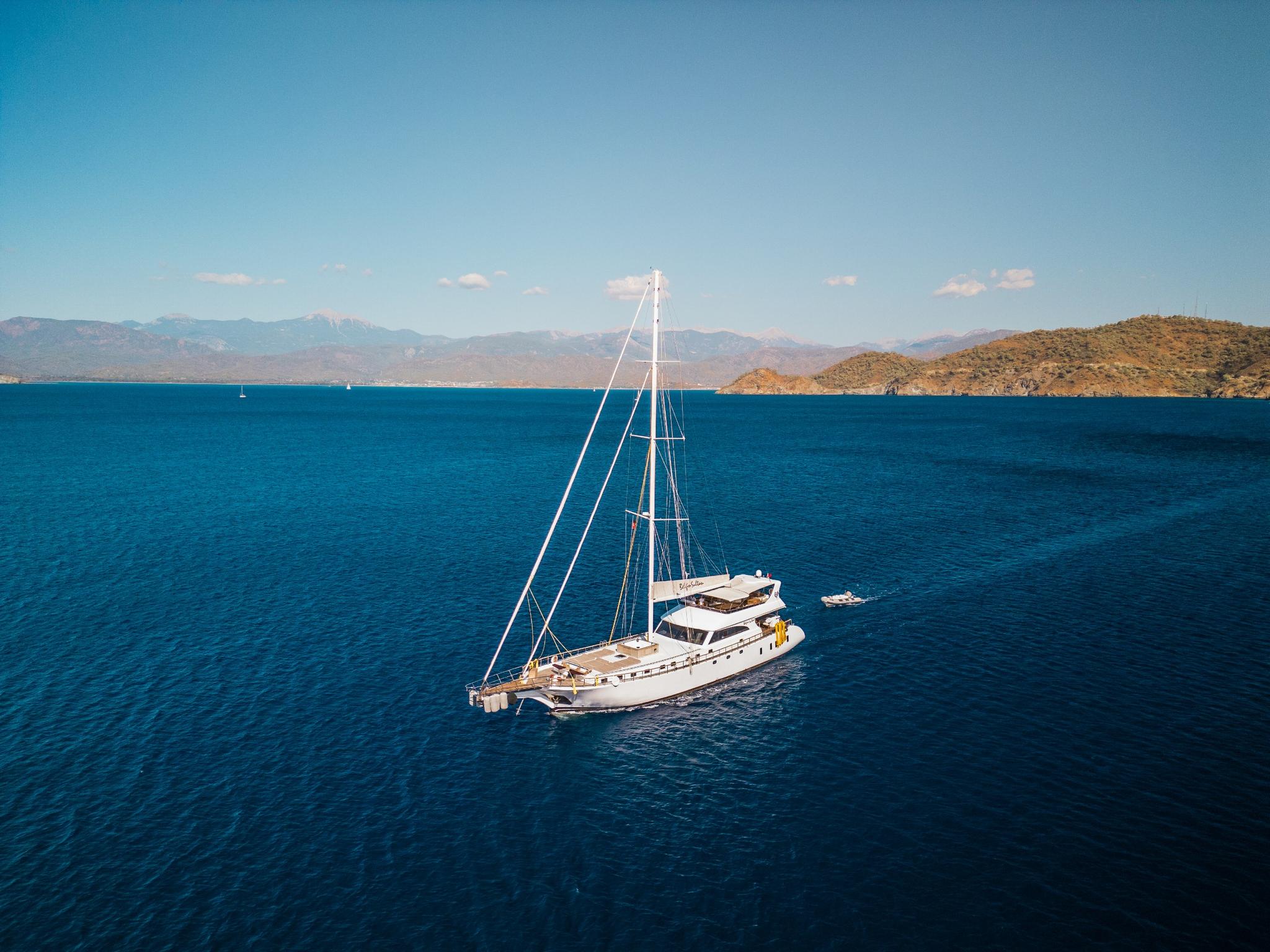 aerial view of white sailing yacht anchored in deep blue Mediterranean waters with mountainous coastline