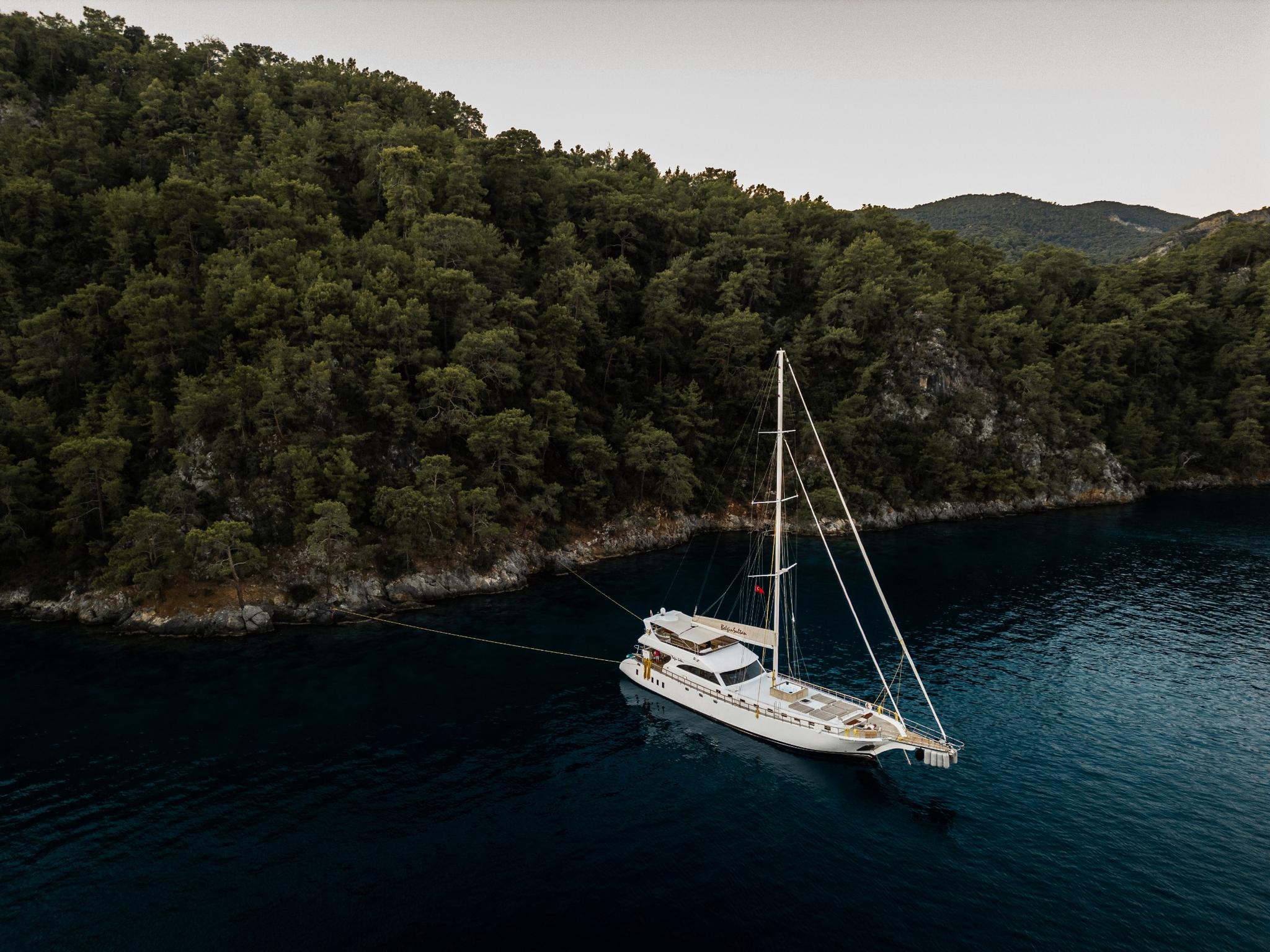 aerial view of white sailing gulet anchored in forested cove with deep blue waters