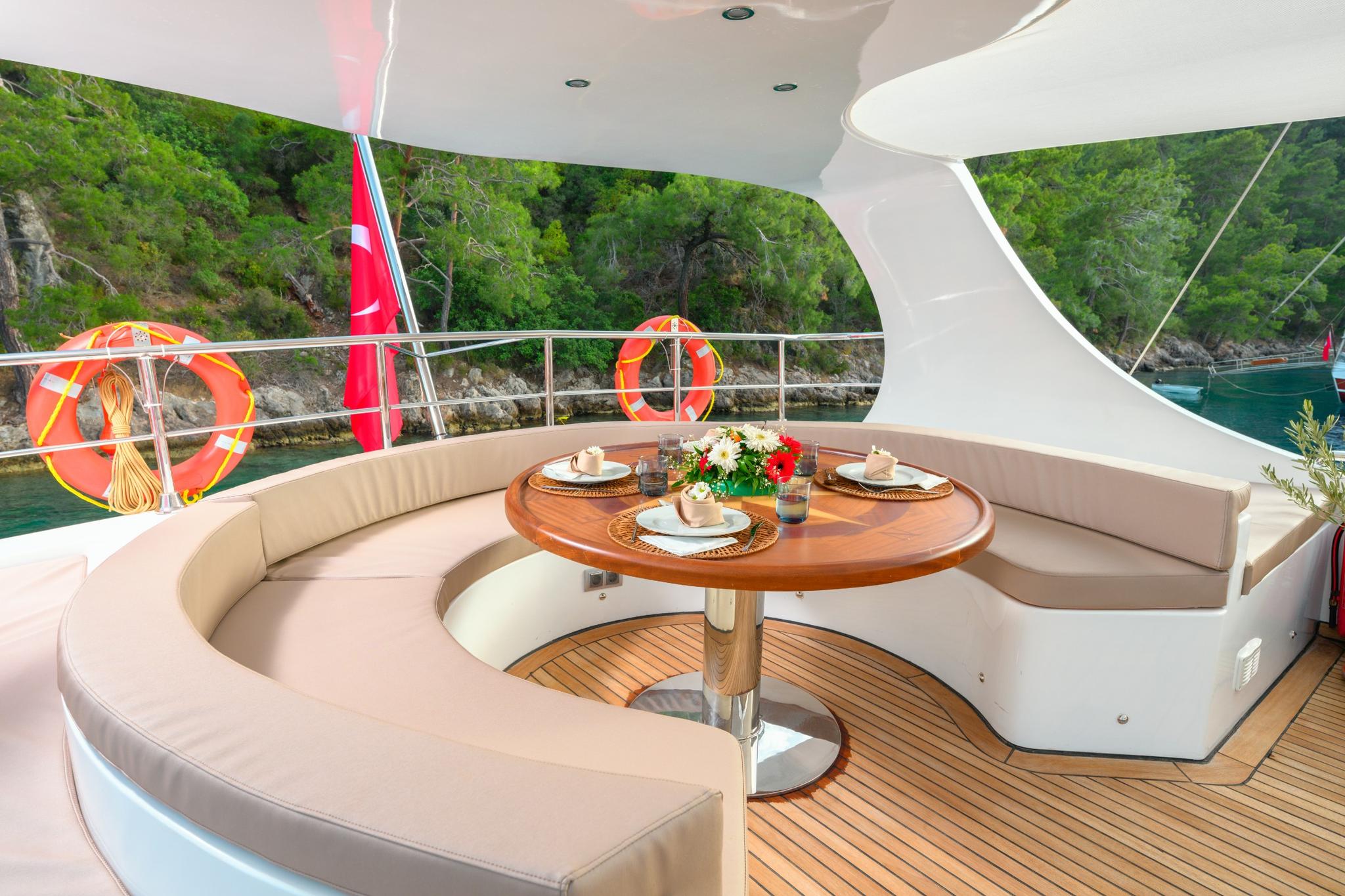 curved cushioned seating with teak dining table on yacht deck overlooking forested coastline