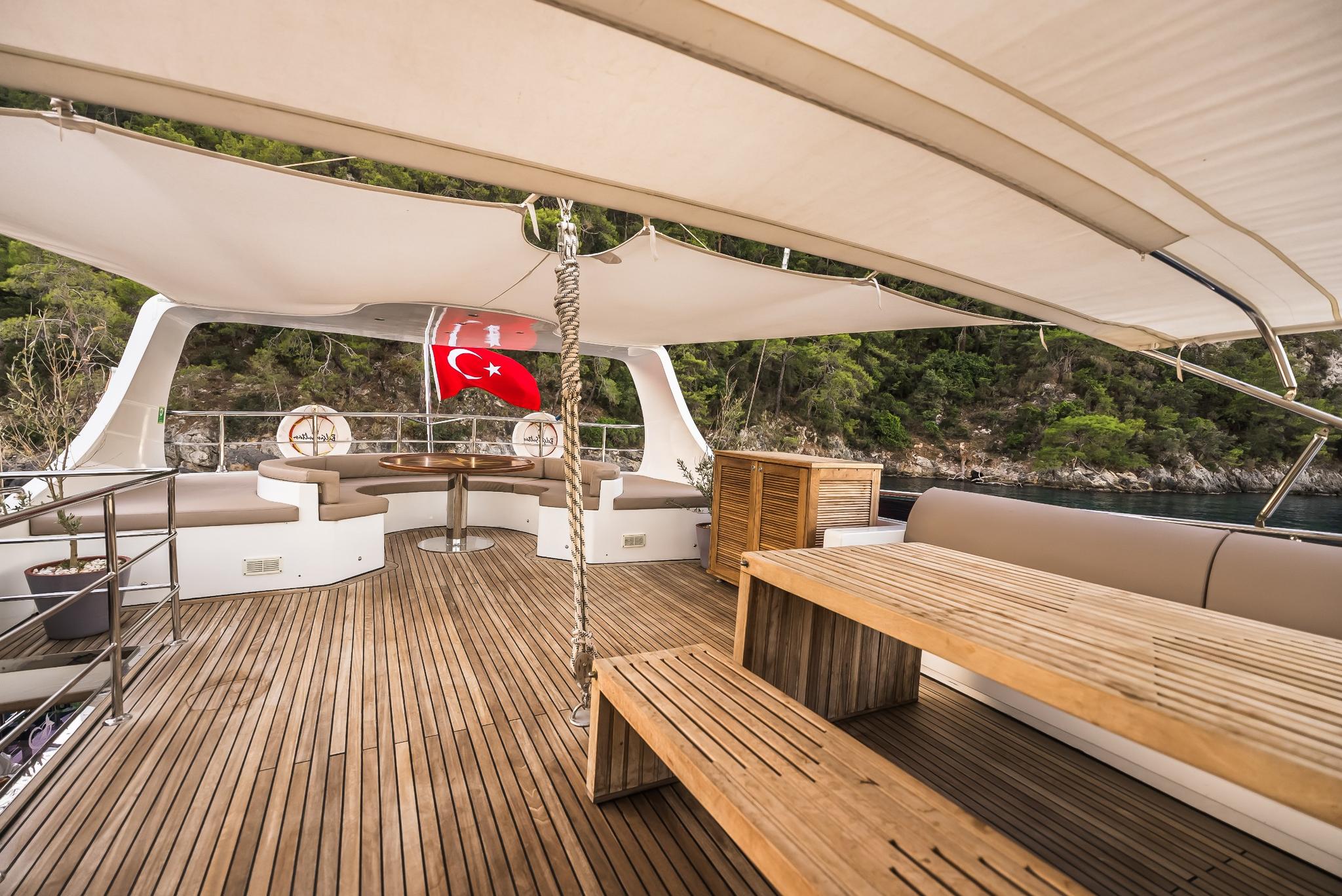 yacht aft deck with teak dining table, built-in seating, Turkish flag and coastal backdrop