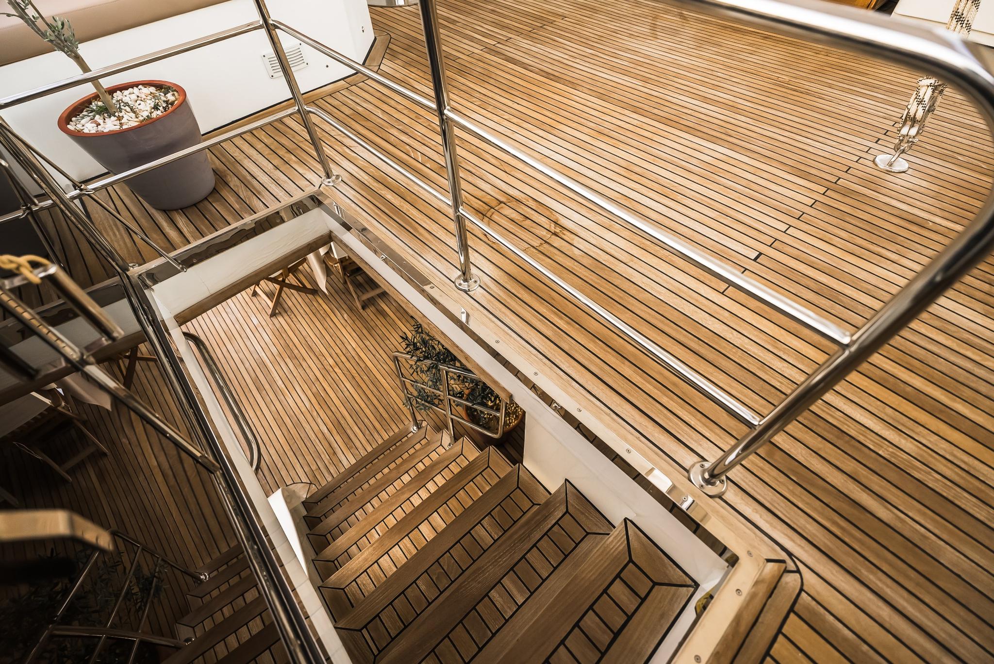 yacht teak deck with wooden staircase descending to lower cockpit level with stainless steel railings