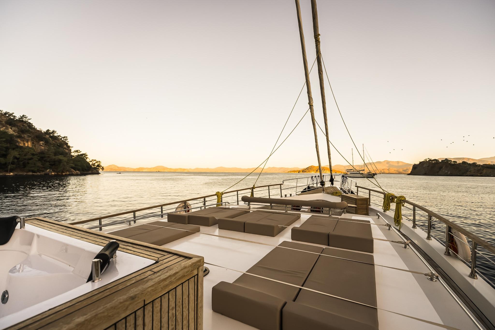 bow deck seating area with beige cushioned loungers and stainless steel railings at sunset