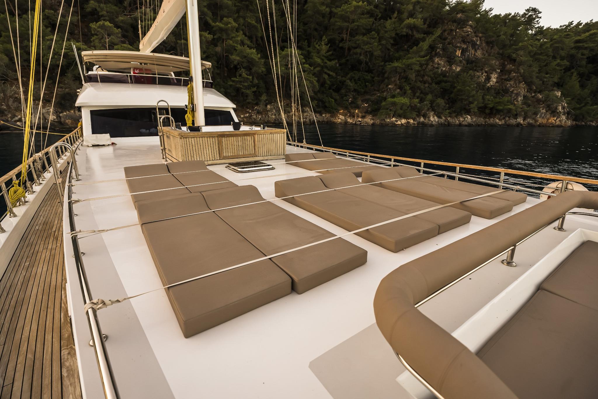 bow sun deck with beige cushioned loungers and curved seating area on luxury gulet