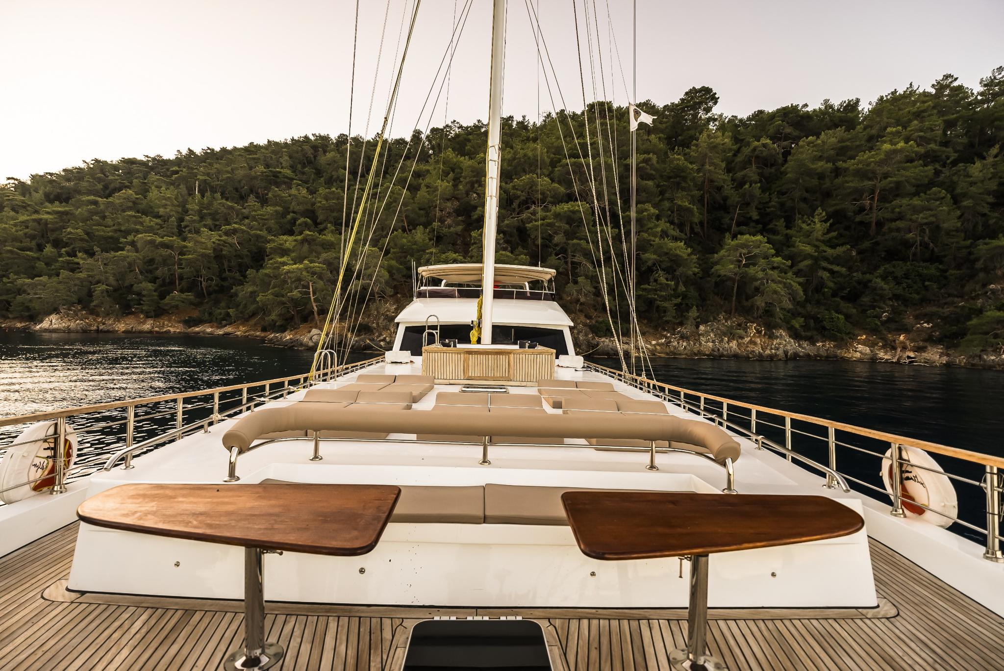 gulet forward deck with wooden dining tables, white seating, and sailing mast rigging