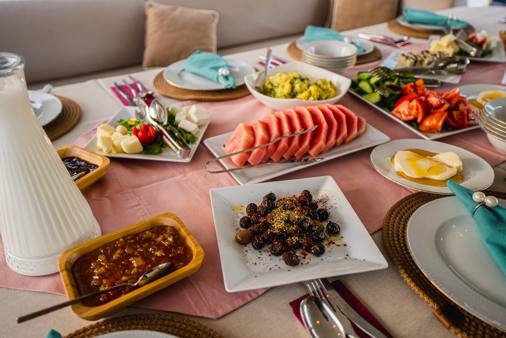 yacht dining table set with breakfast spread including watermelon, olives, cheese and preserves