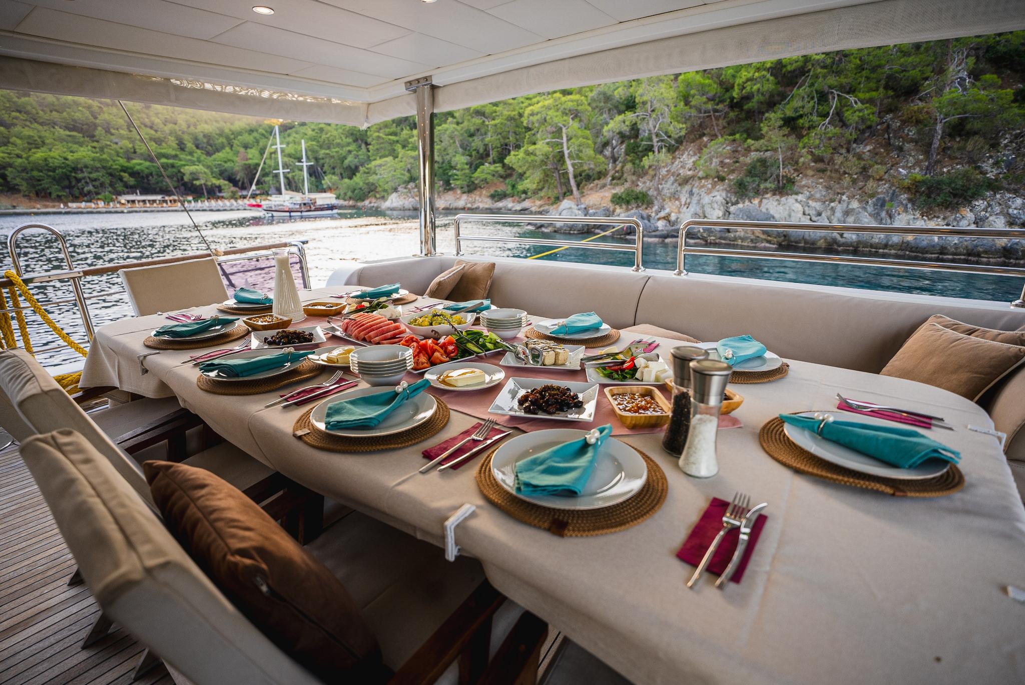 yacht aft deck dining table set with Mediterranean cuisine and turquoise napkins overlooking bay