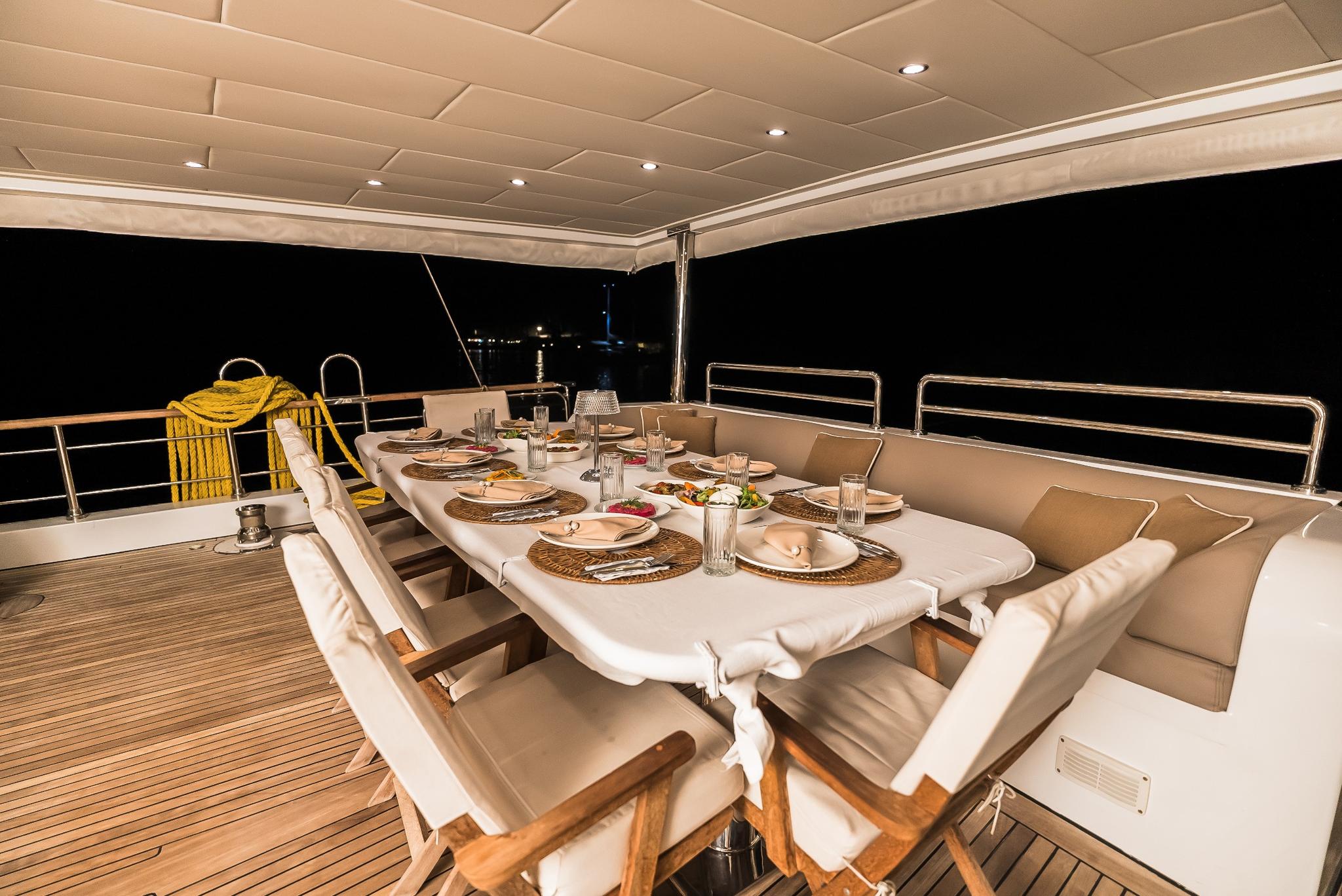 yacht aft deck dining table set with plates and food served at night