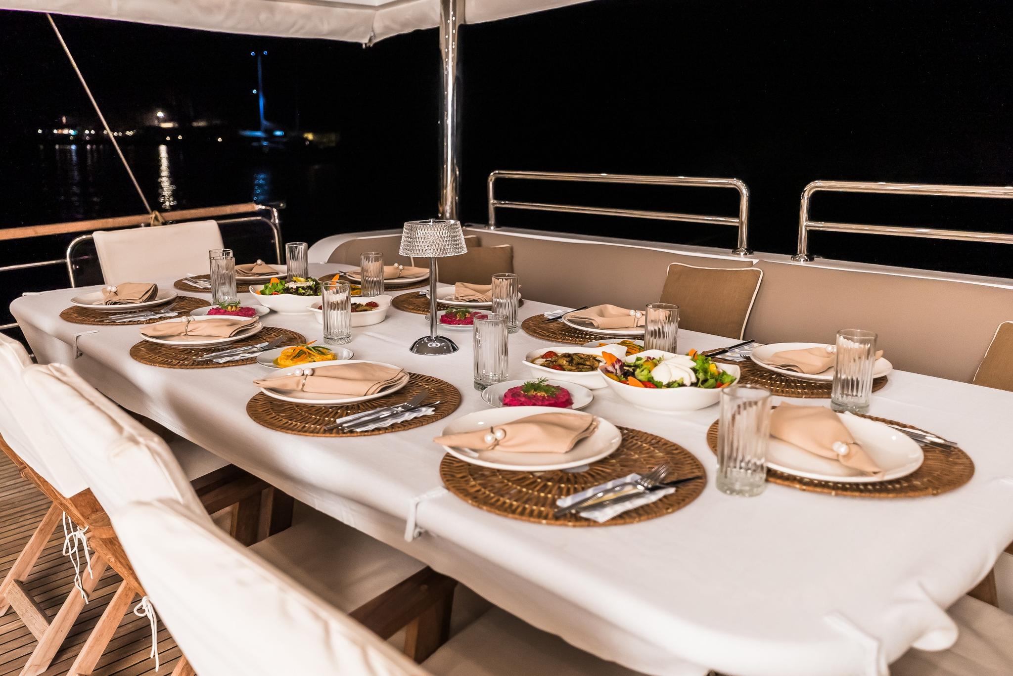 yacht aft deck dining table set with Mediterranean dishes, woven placemats, and glassware at night