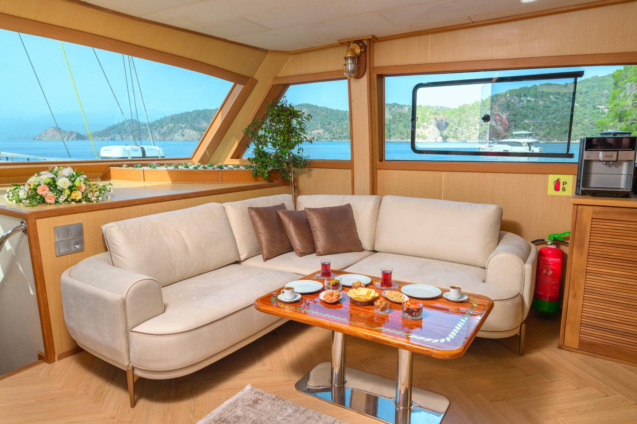yacht salon interior with beige L-shaped sofa, dining table set with food, drinks and plates