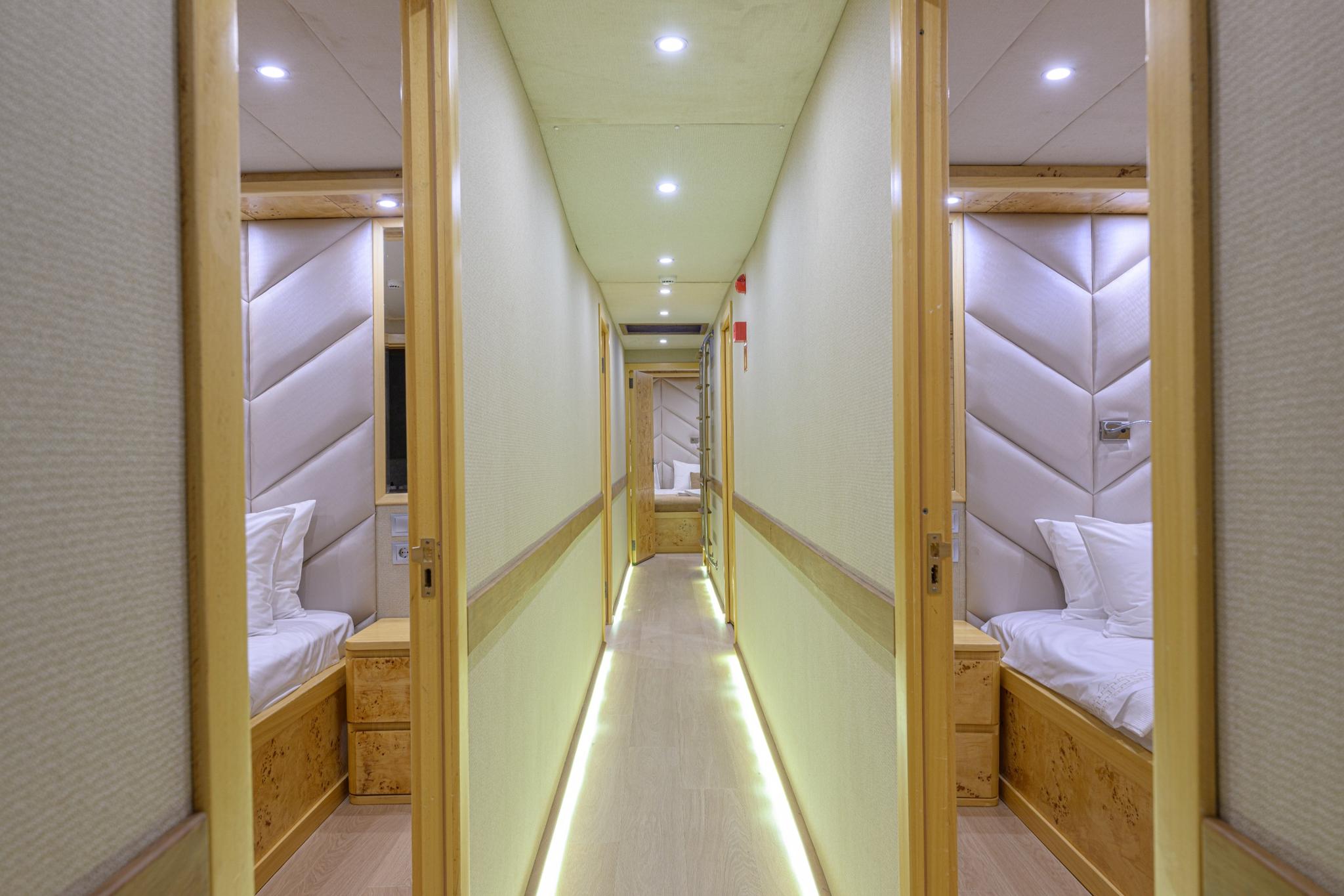 yacht accommodation corridor with open cabin doors showing beds and upholstered headboards