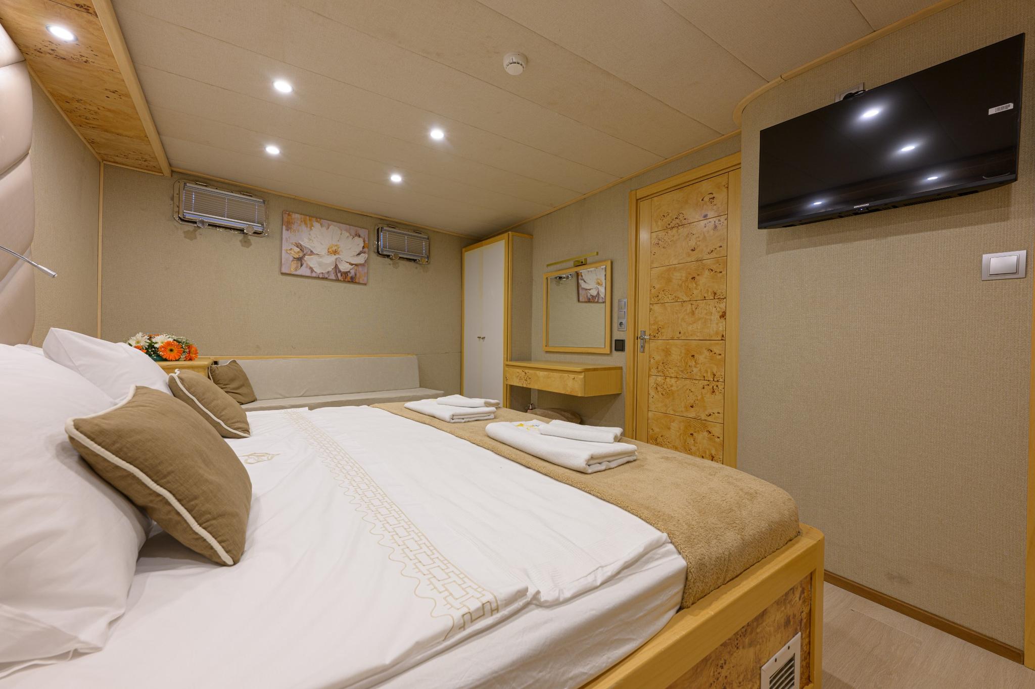 yacht guest cabin with double bed, burled wood paneling, wall-mounted TV and vanity area