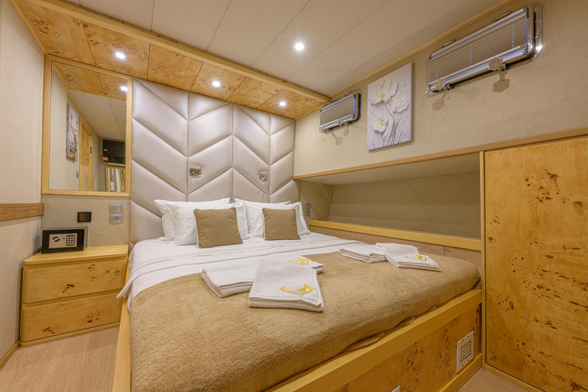 yacht guest cabin featuring double bed with geometric upholstered headboard and burr wood paneling