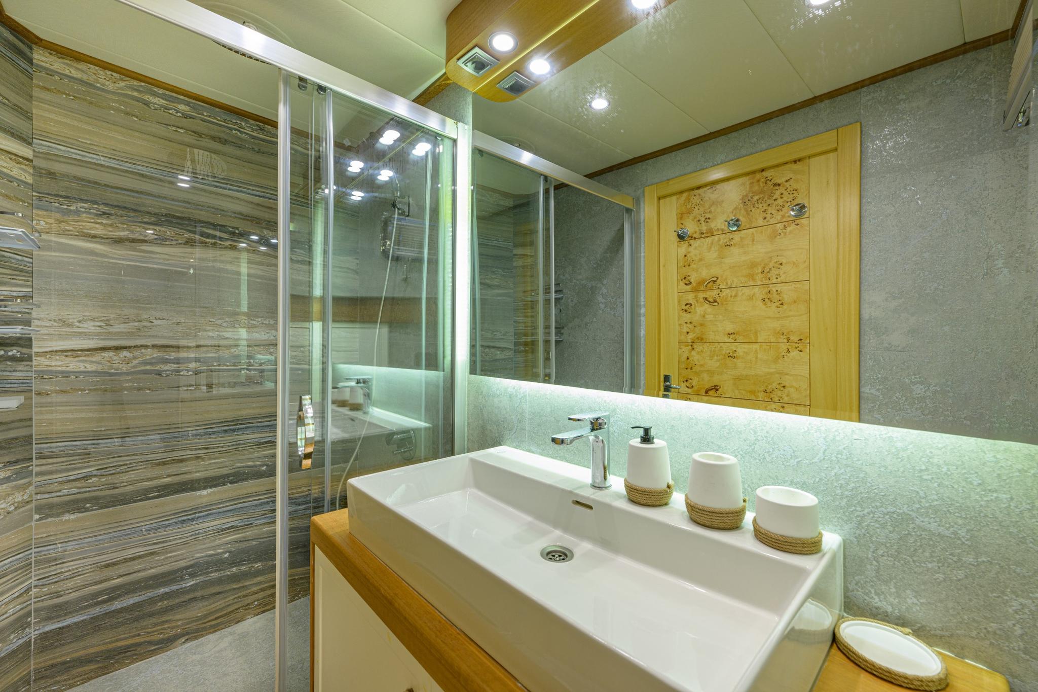 yacht bathroom featuring glass shower enclosure, white ceramic sink with chrome faucet and illuminated mirror