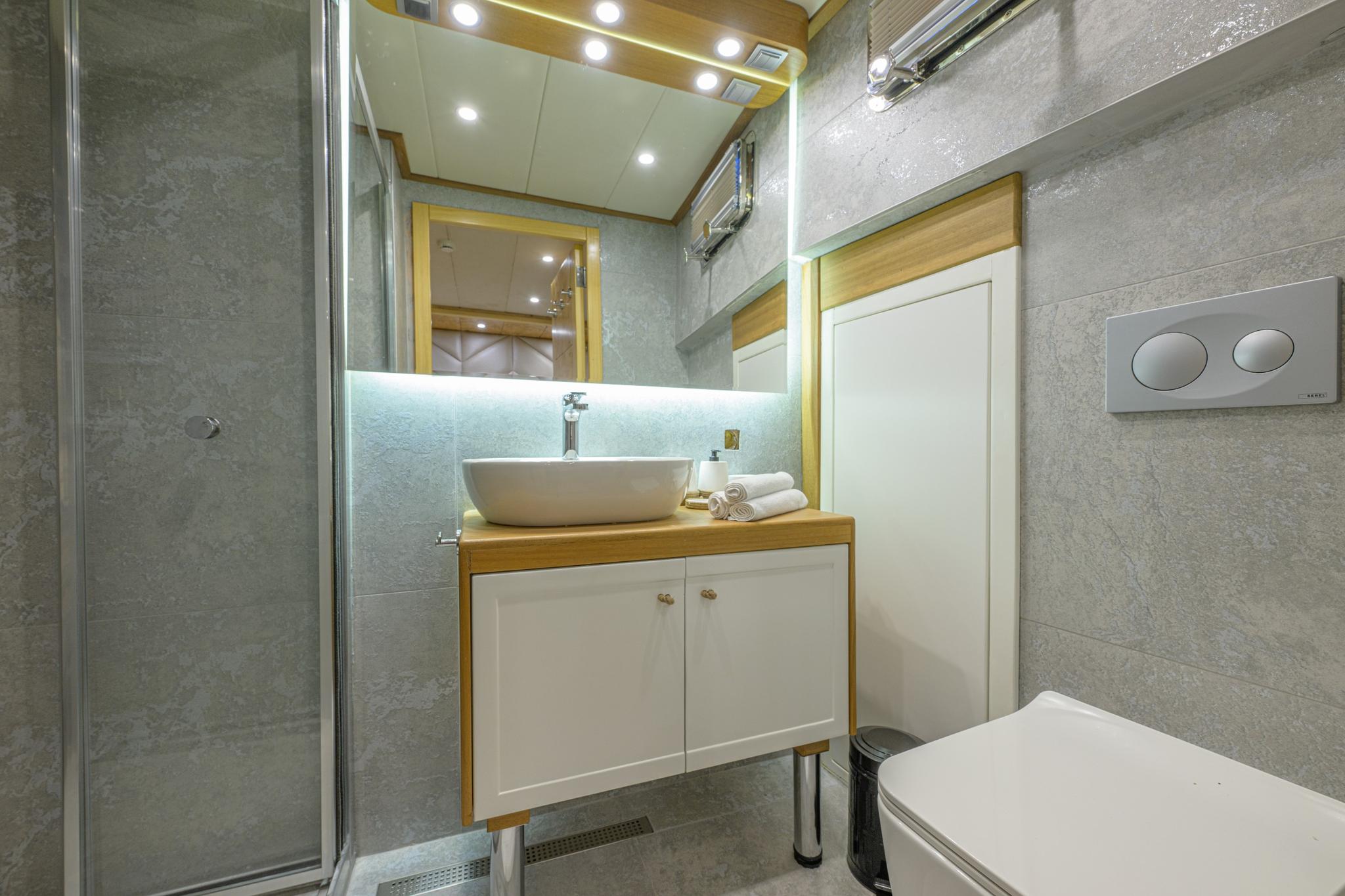 modern yacht guest bathroom featuring white vessel sink, glass shower enclosure, and grey marble tiles