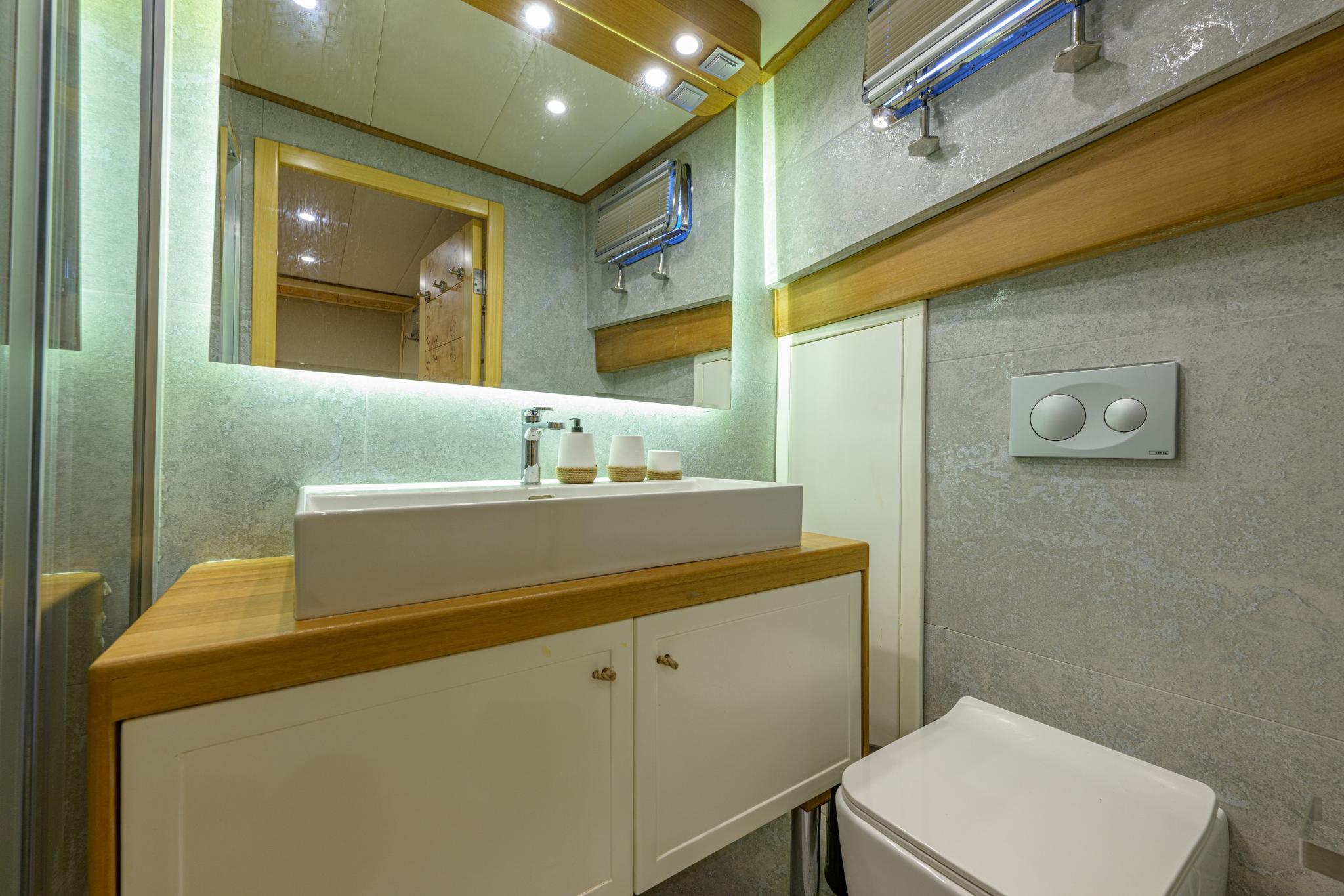 modern yacht bathroom featuring rectangular vessel sink, LED mirror lighting, and wall-mounted toilet