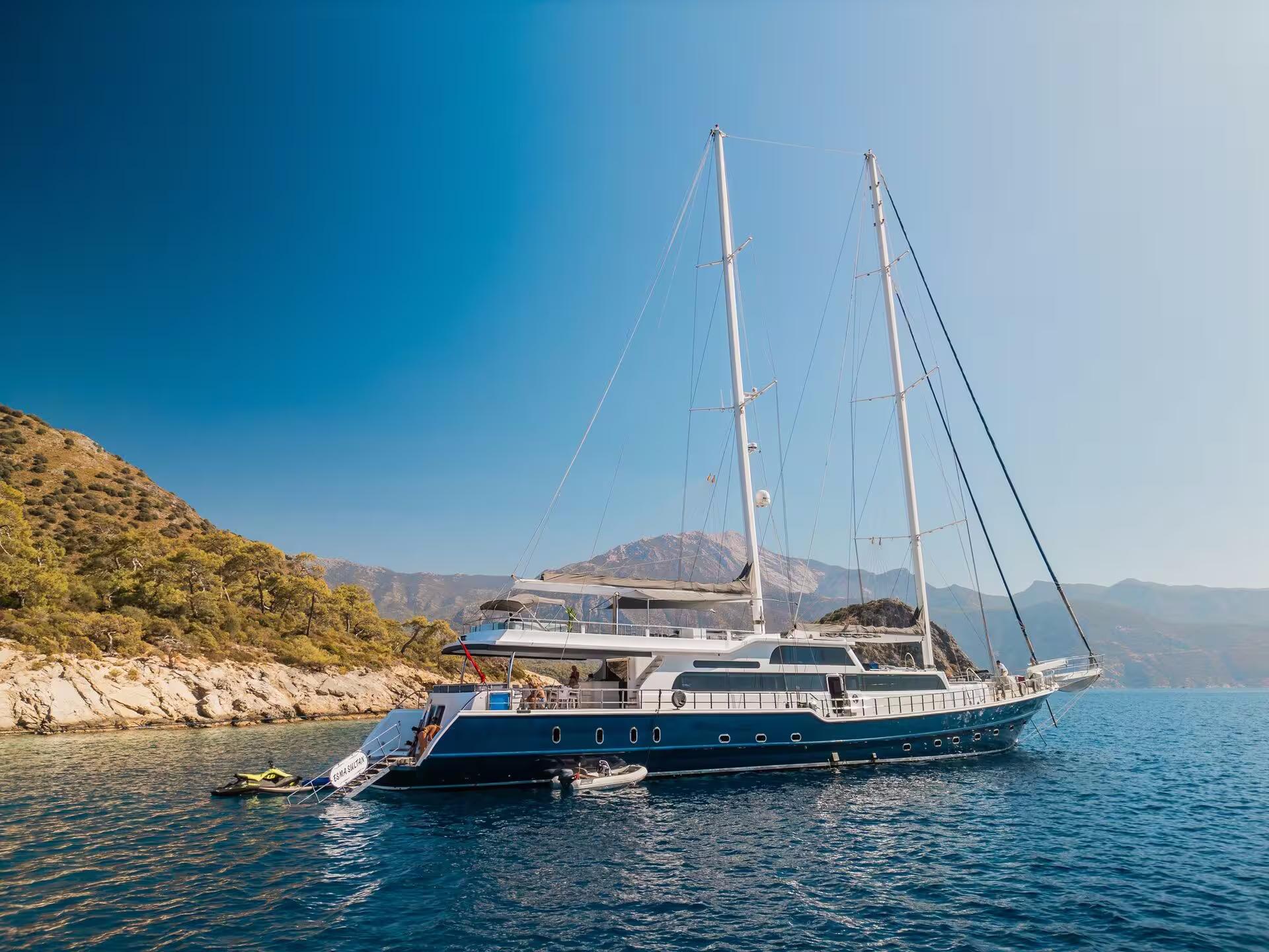 luxury gulet yacht anchored in turquoise Mediterranean bay with rocky coastline and mountains
