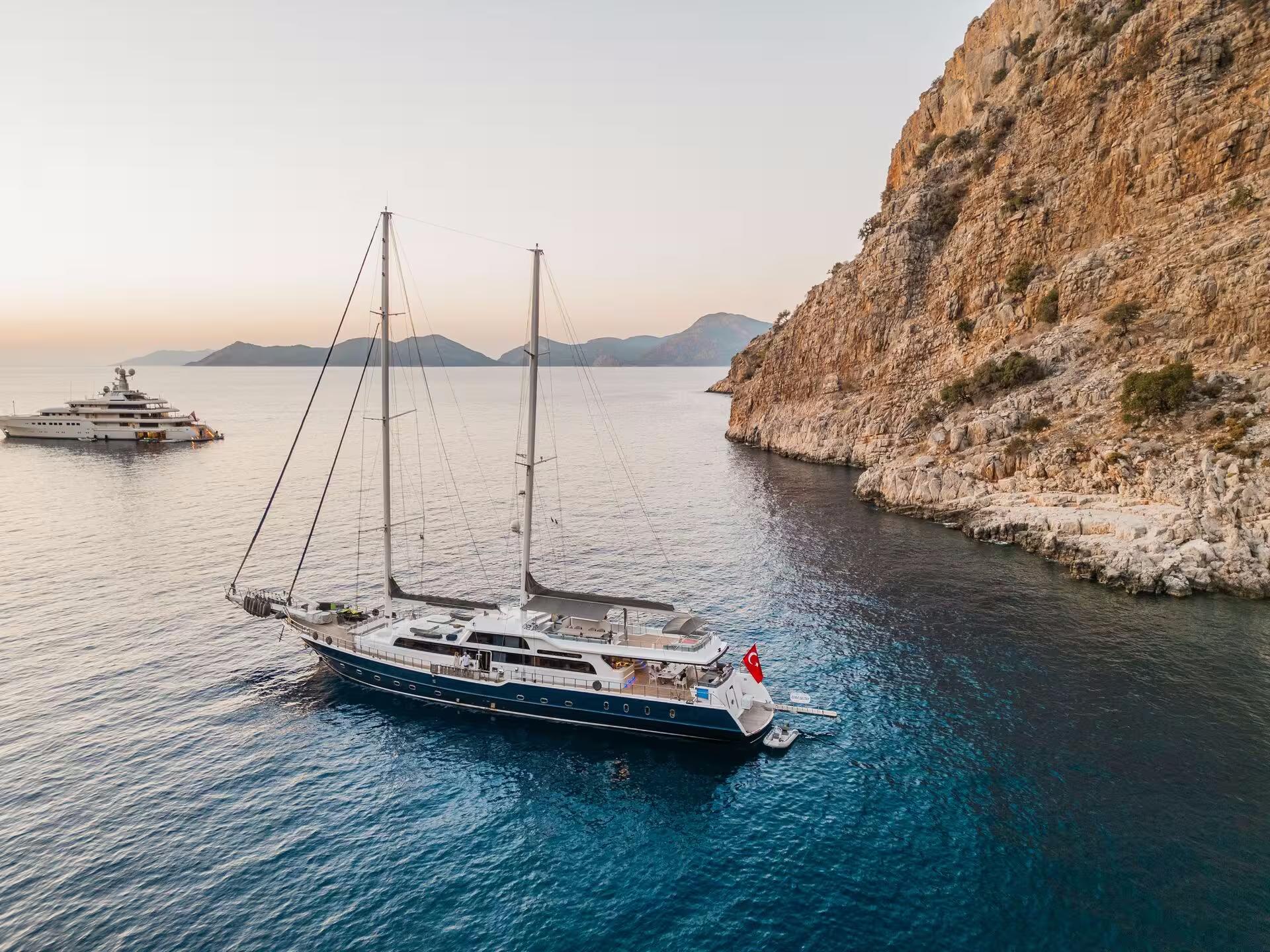 aerial view of blue-hulled sailing yacht anchored in turquoise waters near dramatic limestone cliffs