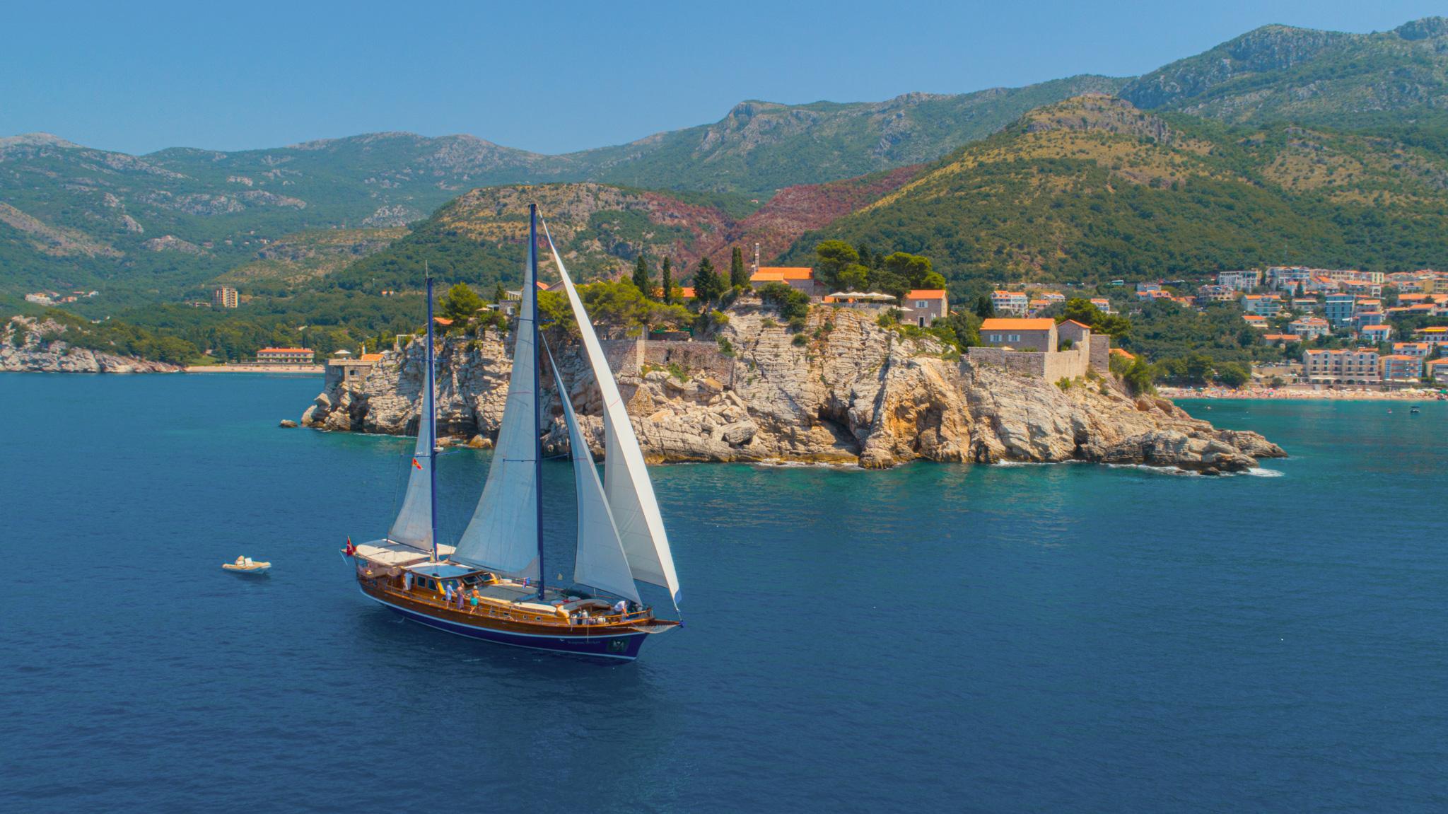 Classic wooden gulet under full sail passing Sveti Stefan rocky islet Montenegro