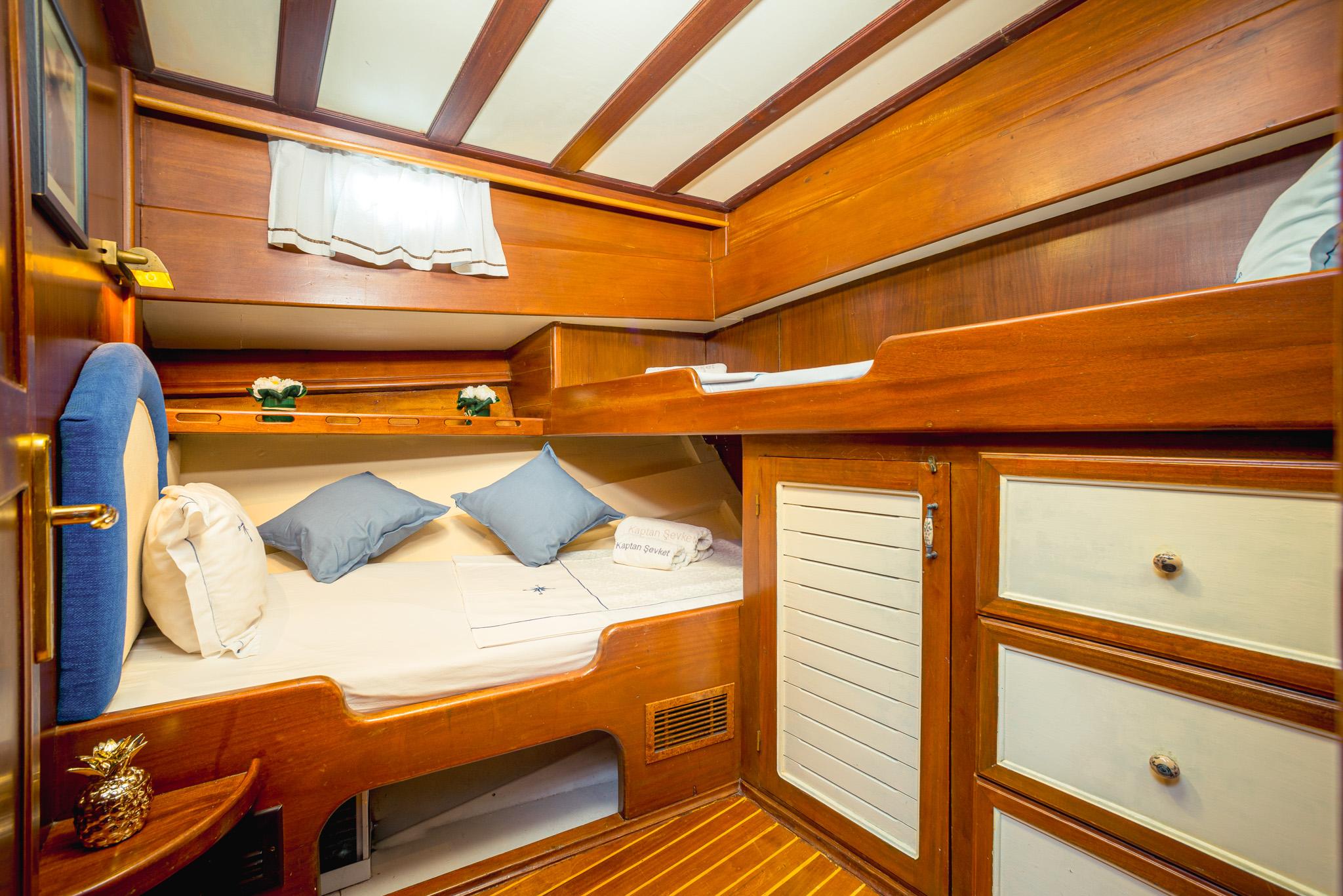 gulet twin bunk cabin with blue accent cushions, warm teak woodwork, and built-in storage drawers
