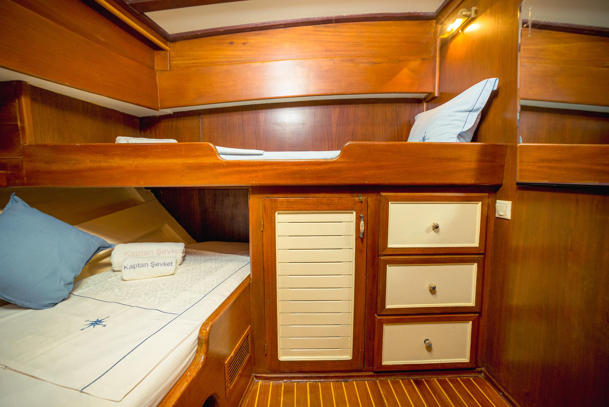 Gulet bunk cabin with two single berths, louvred storage cupboard and three cream drawers, branded Kaptan Sevket towels on lower bunk