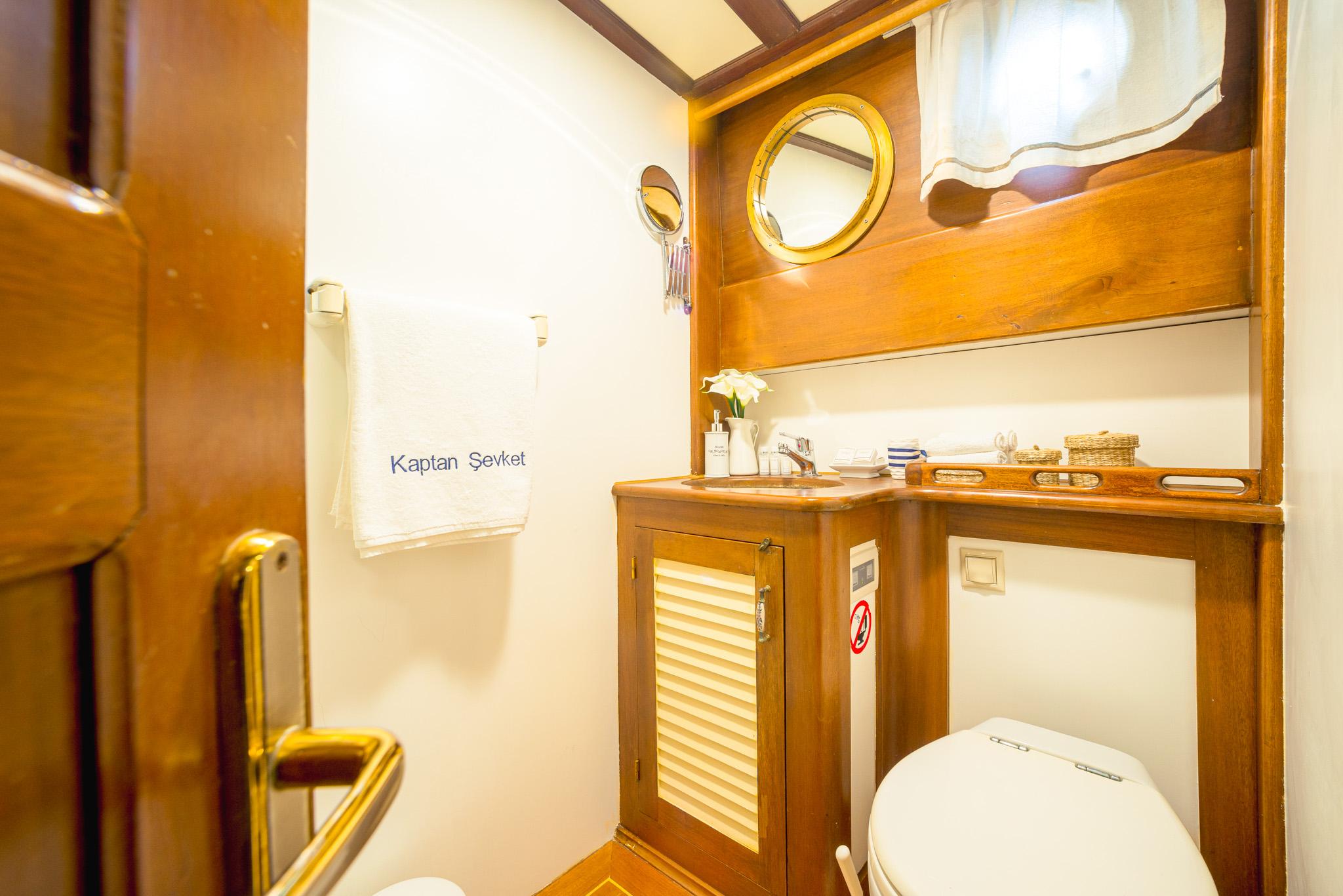 Gulet Kaptan Sevket en-suite bathroom with wooden vanity unit, brass porthole mirror, and white toilet